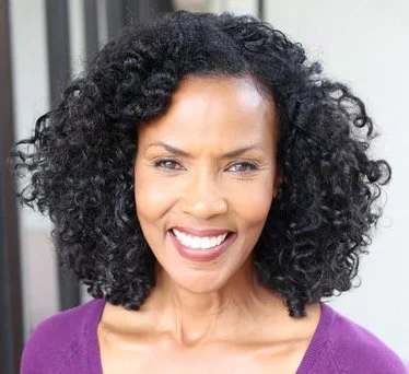 A woman with curly black hair smiling and wearing a purple top.