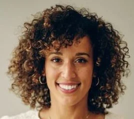 Close-up of a smiling woman with curly hair and hoop earrings