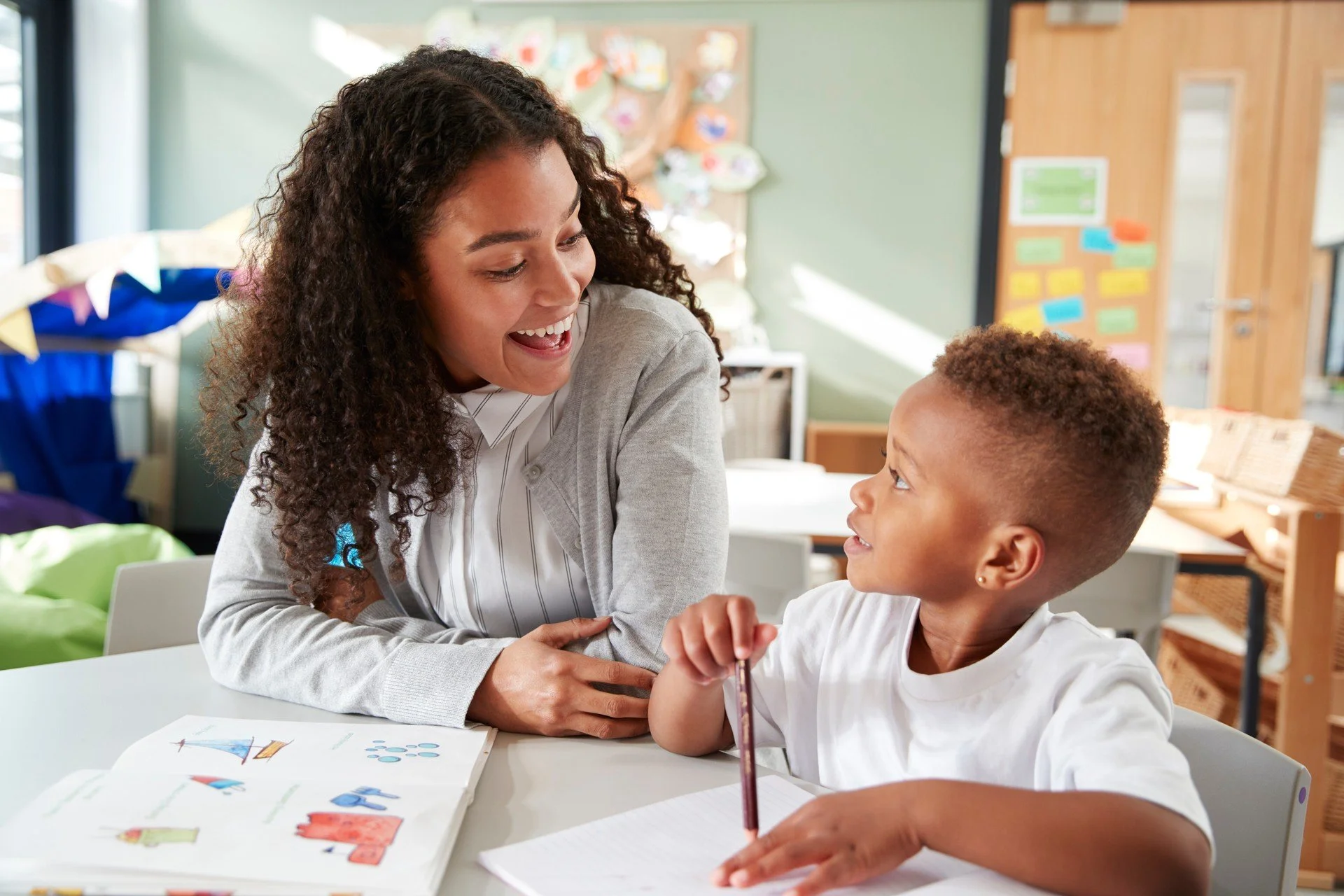 Teacher laughing with young student holding a pen