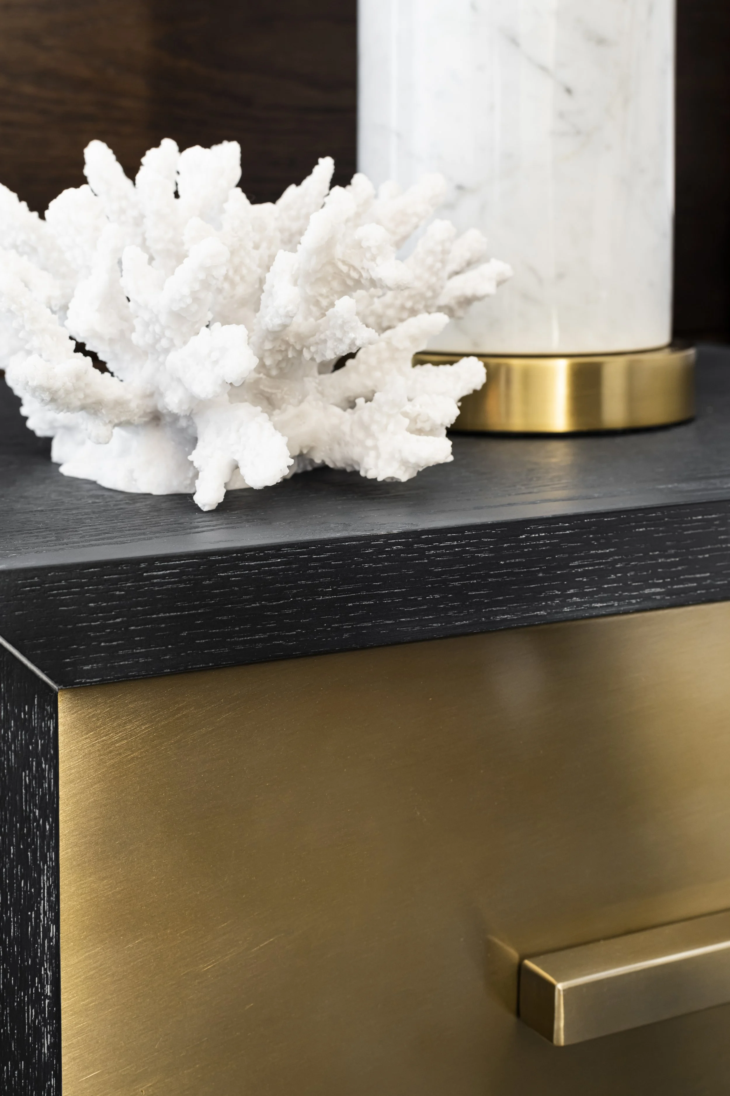 A white coral sculpture on a dark wooden surface near gold-colored and white marble decorative objects.