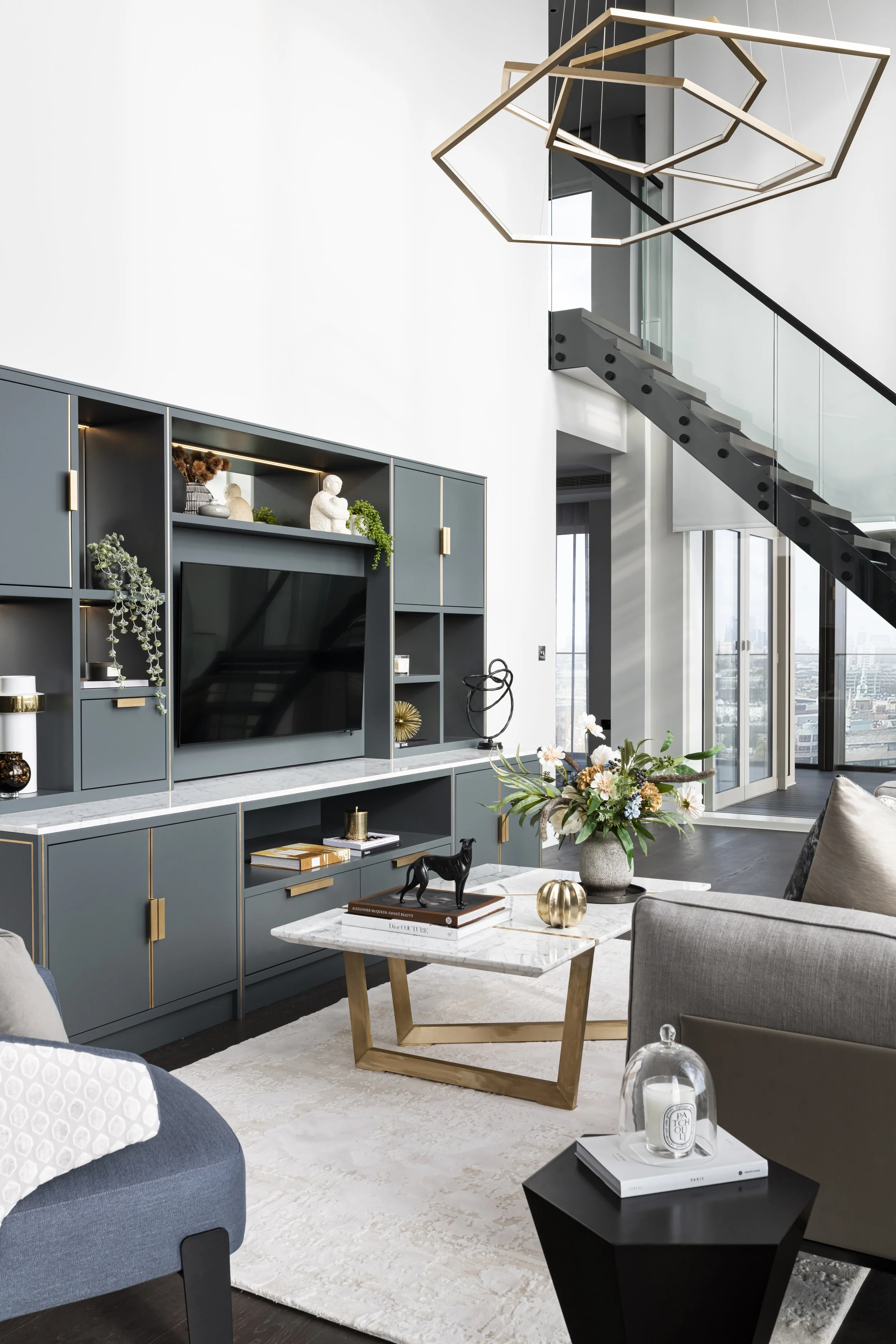 Modern living room with blue media wall unit, coffee table with floral arrangement, blue armchair, and black side table with a glass dome and candle inside.