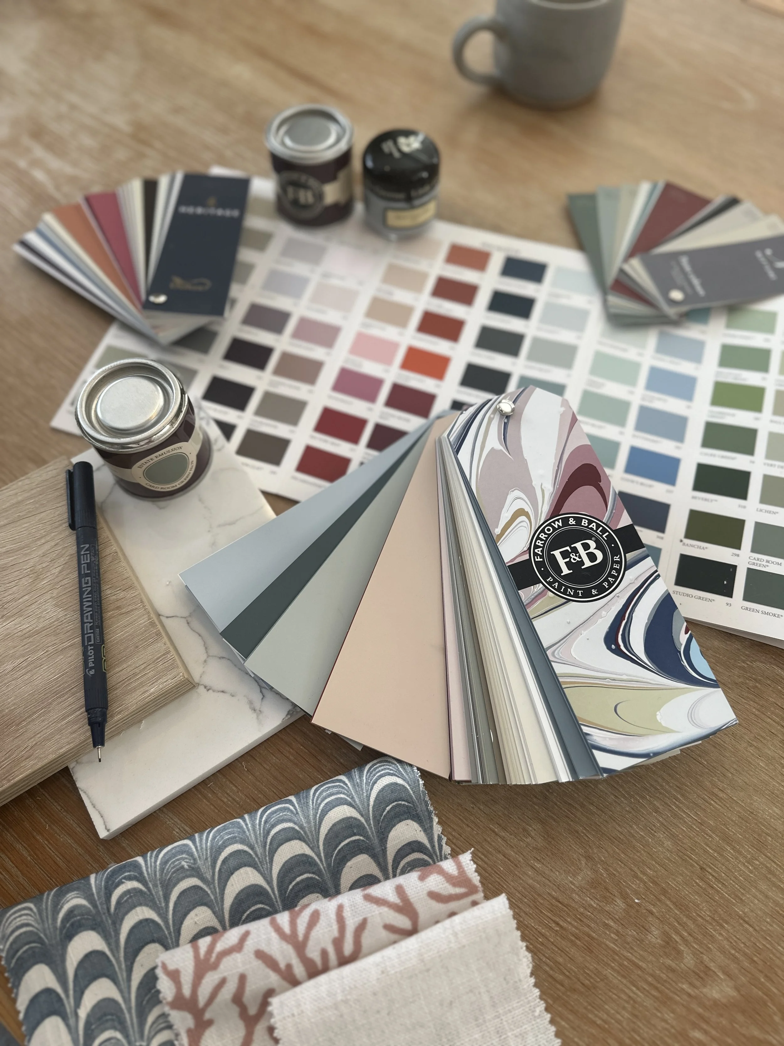 Interior design color and paint samples, fabric swatches, and paint cans on a wooden table.