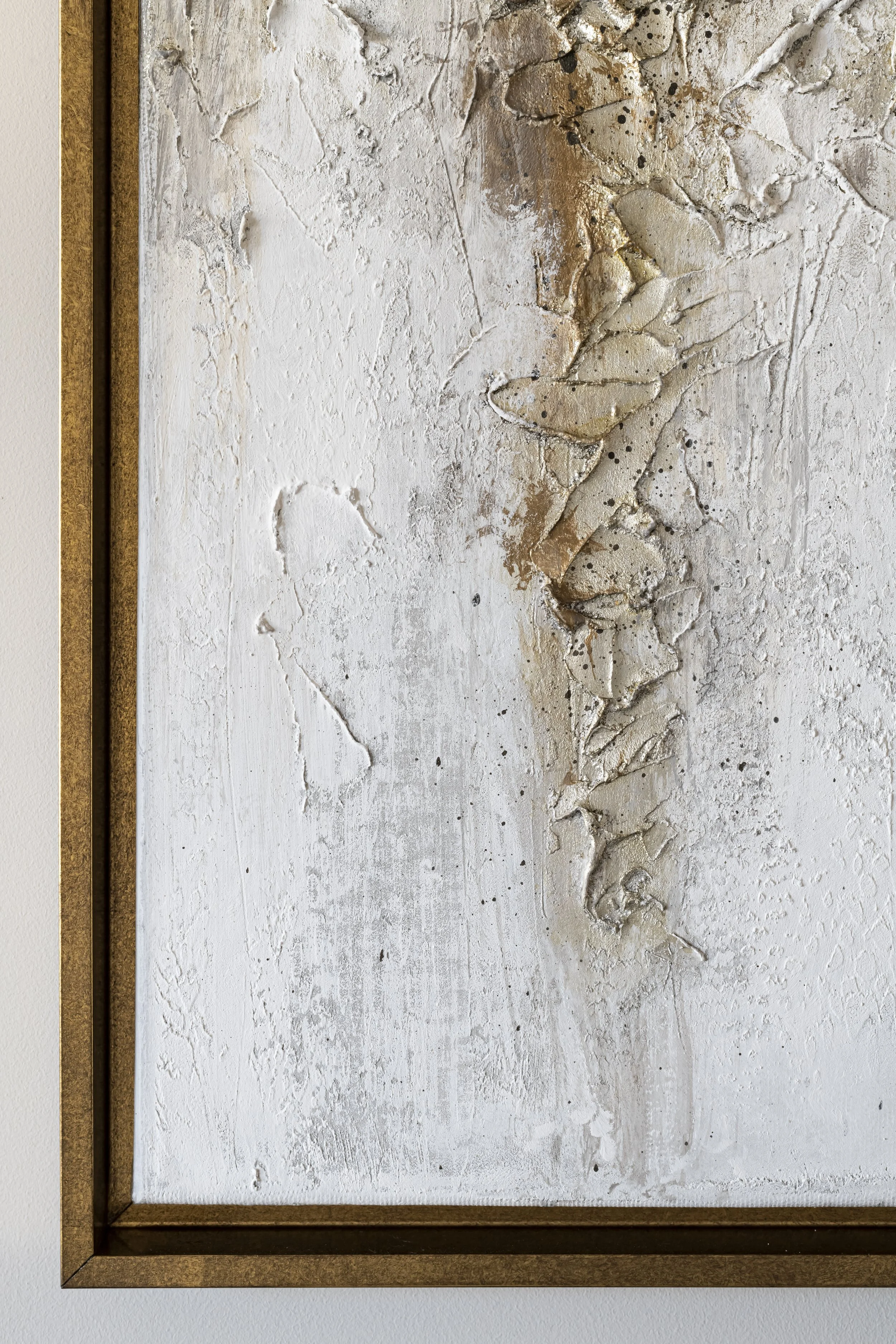 A textured piece of art with abstract raised patterns in white, beige, and gold tones, framed in a gold-colored border.