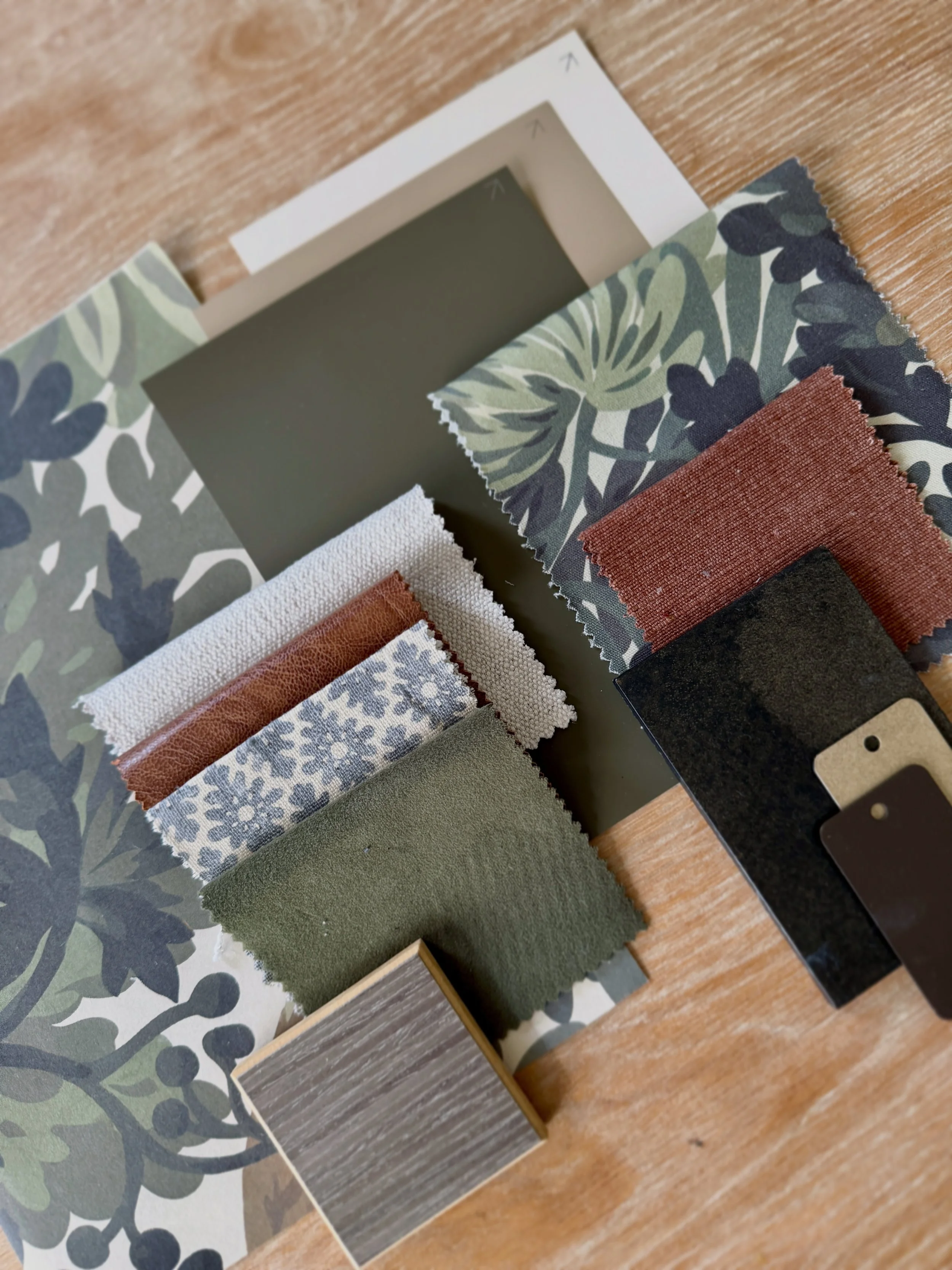 Various fabric swatches with different textures and colors, including floral, solid green, brown leather, and wood-patterned designs, placed on a wooden surface.