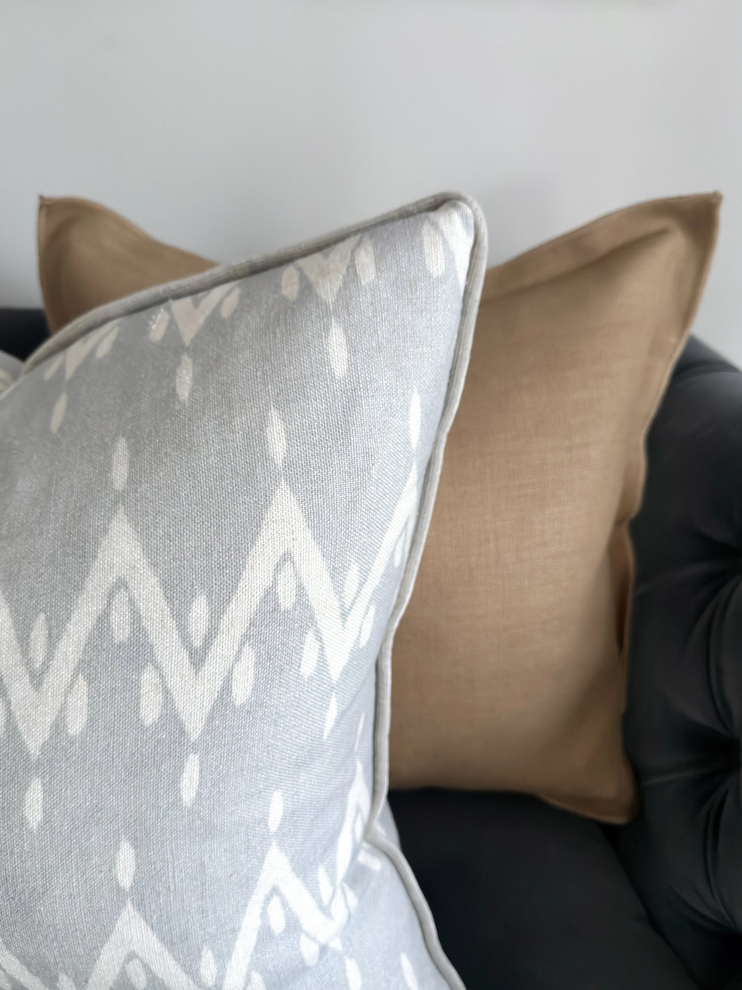Close-up of three decorative cushions on a sofa, with one cushion in the foreground having a light blue pattern and two plain cushions in caramel and slate grey in the background.