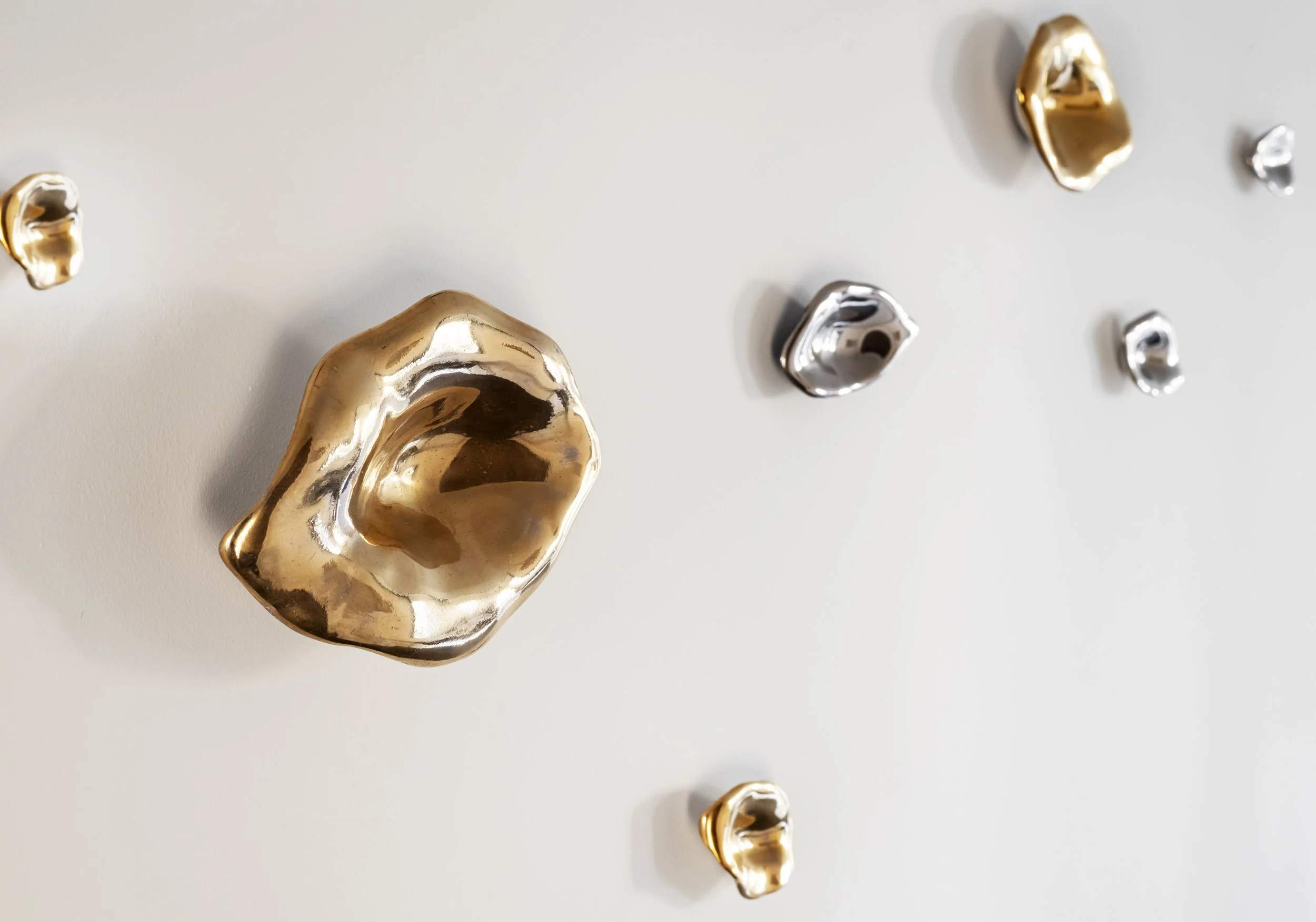 Various metallic objects, including gold and silver-colored irregularly shaped pieces and small round pieces, arranged on a plain surface.