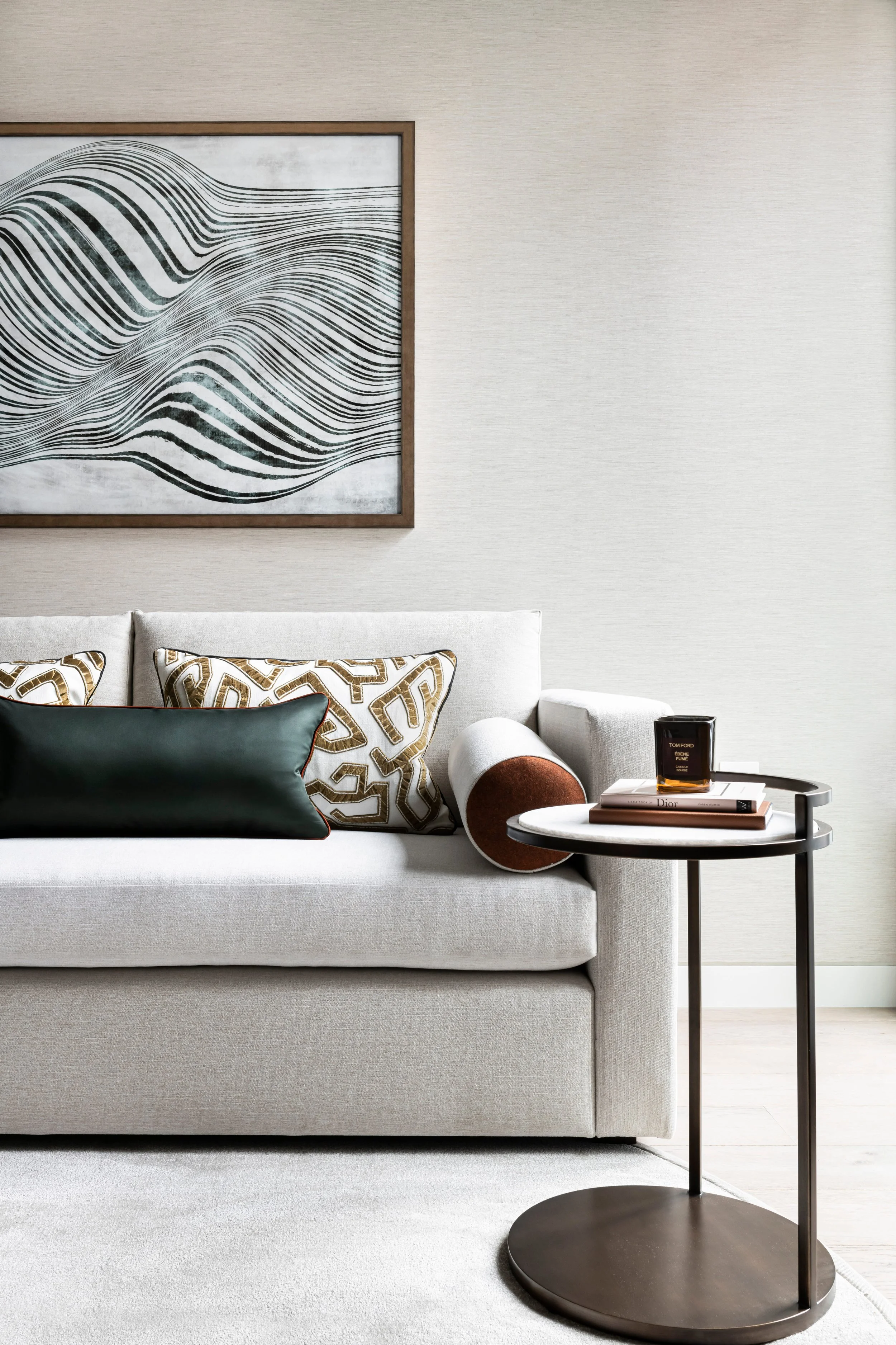 Modern living room with a neutral sofa, decorative cushions, abstract art on the wall and a side table with books and a candle.