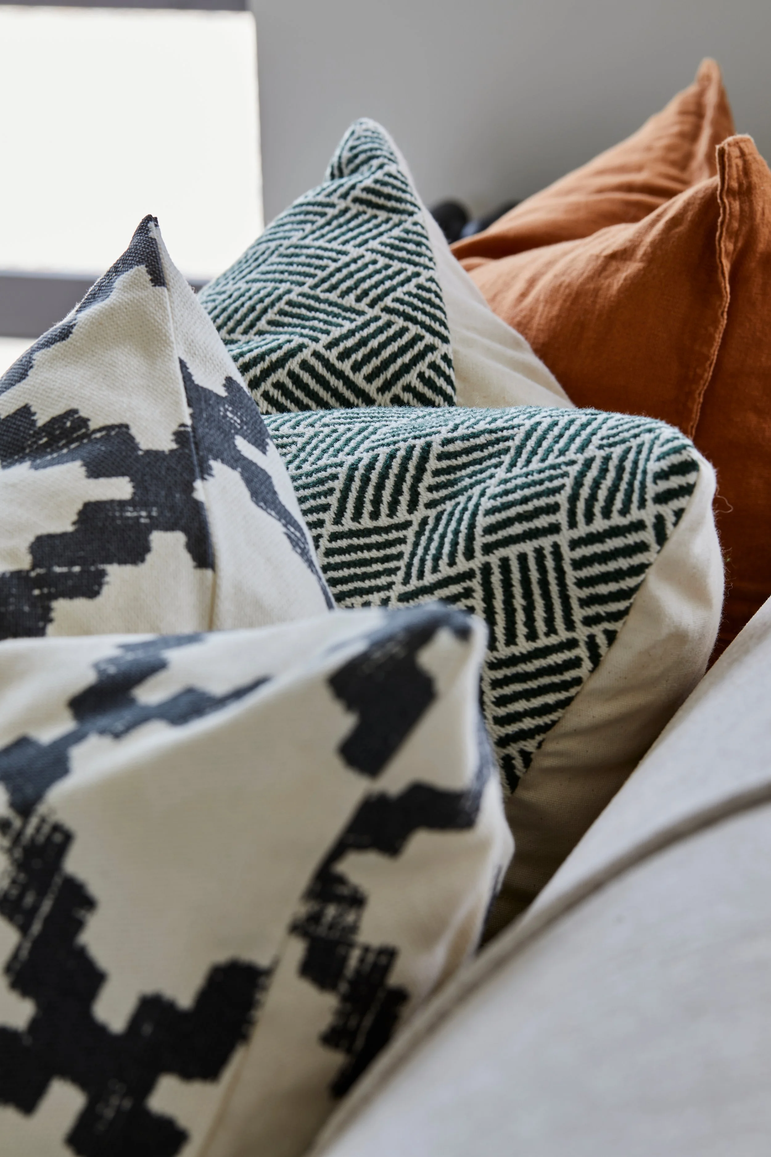 Close-up of decorative cushiosn with various black, white, and brown patterns and textures, arranged on a sofa.