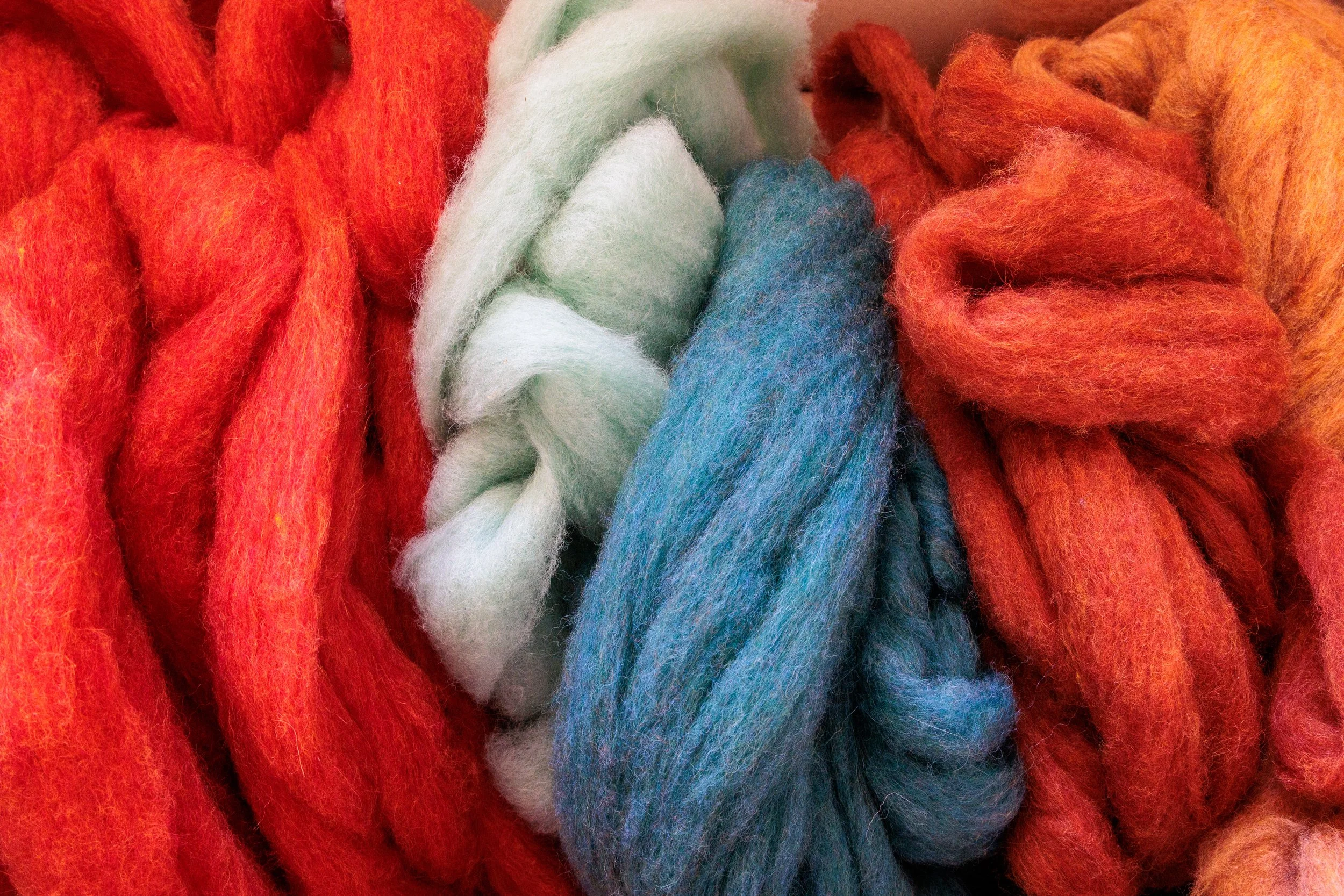 Close-up of chunky, multicolored knitted wool yarn in shades of orange, white, green, and blue.