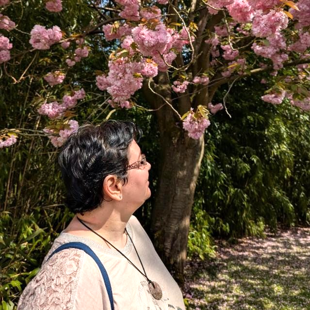 Frau mit dunklen Haaren und Brille steht neben einem blühenden Kirschbaum