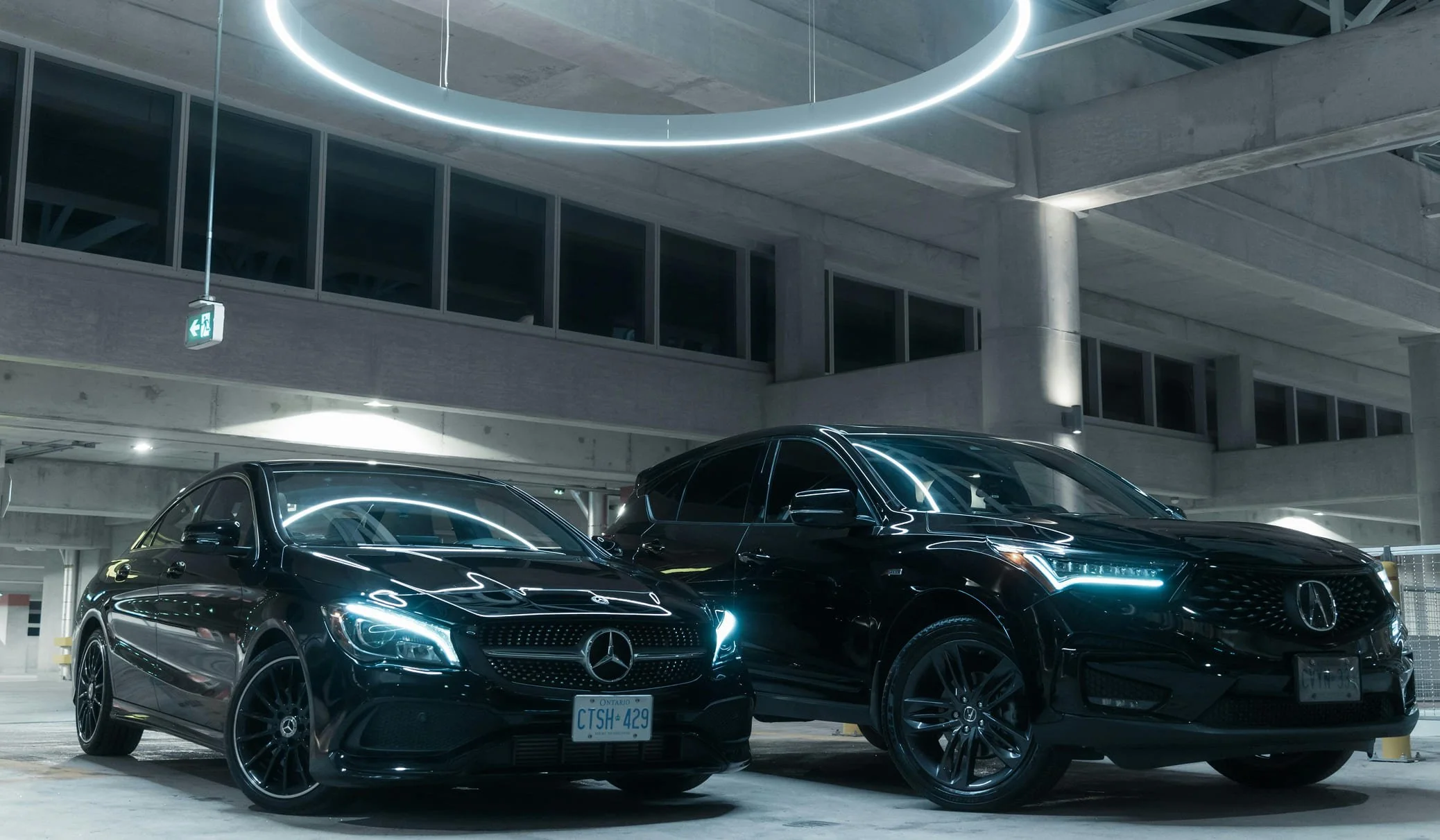 Two black Mercedes-Benz cars parked in an indoor parking garage with modern lighting and concrete structure.