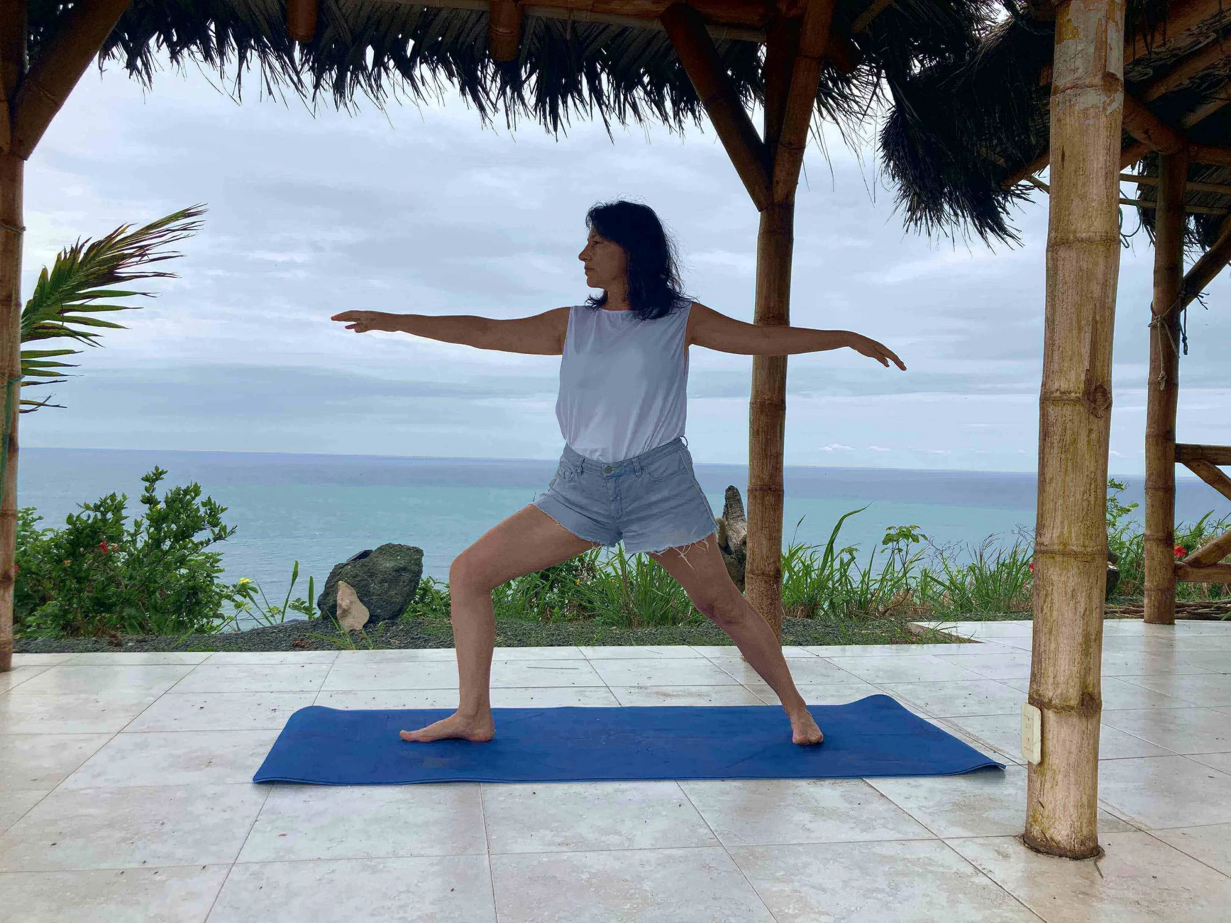 La terapeuta Verónica Ávila realizando la postura de yoga del guerrero frente al mar; una práctica de enraizamiento y fuerza que integra cuerpo y mente en su filosofía de trabajo.