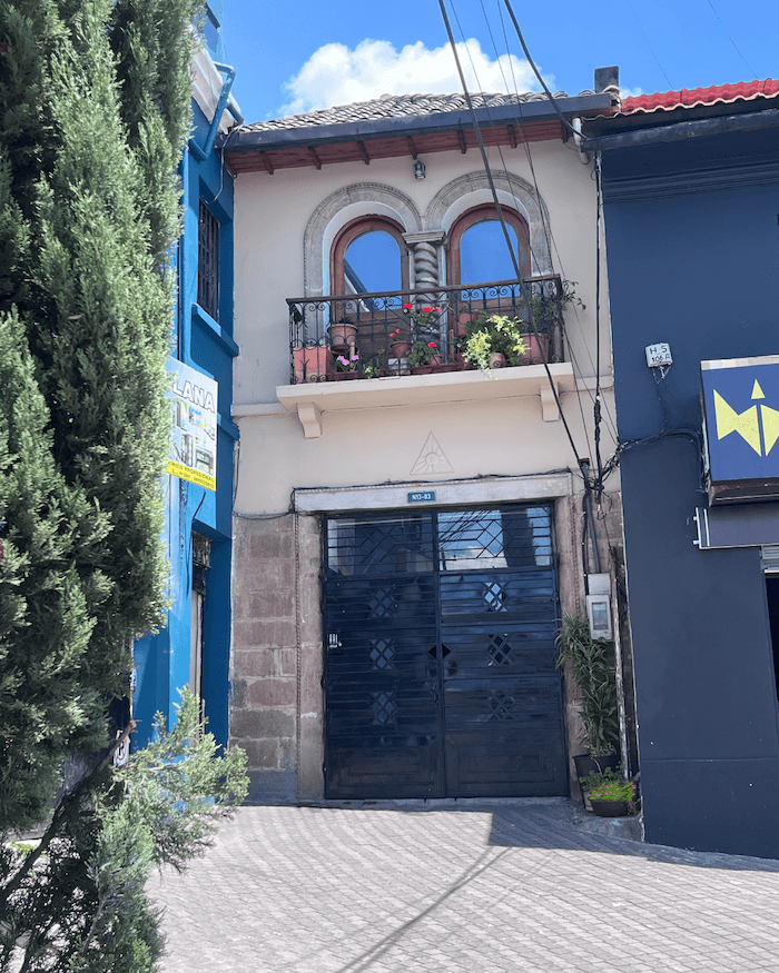 Fachada del consultorio de Verónica Ávila en Quito, una casa clara entre edificios azul y negro, con plantas a la entrada.