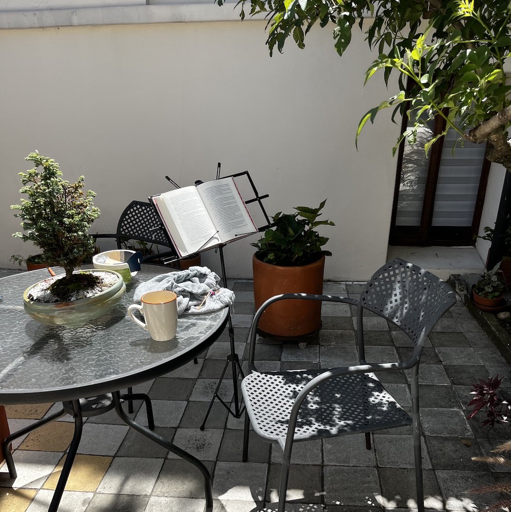 Espacio de descanso con tejido manual, una taza de té y libros al aire libre; reflejo del autocuidado y la vida consciente que promueve Verónica Ávila.