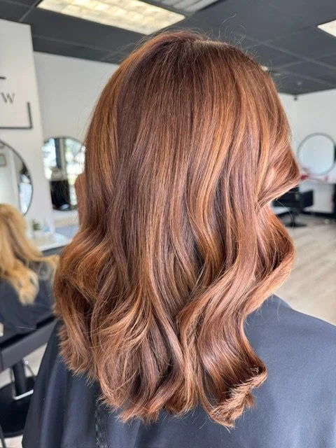 Close-up of a woman's shoulder-length, wavy, reddish-brown hair in a salon.