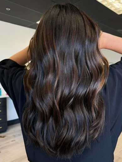 Back view of a person with long, wavy, dark brown hair.
