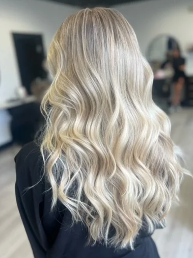 Back view of a woman with long, wavy, blonde hair in a salon