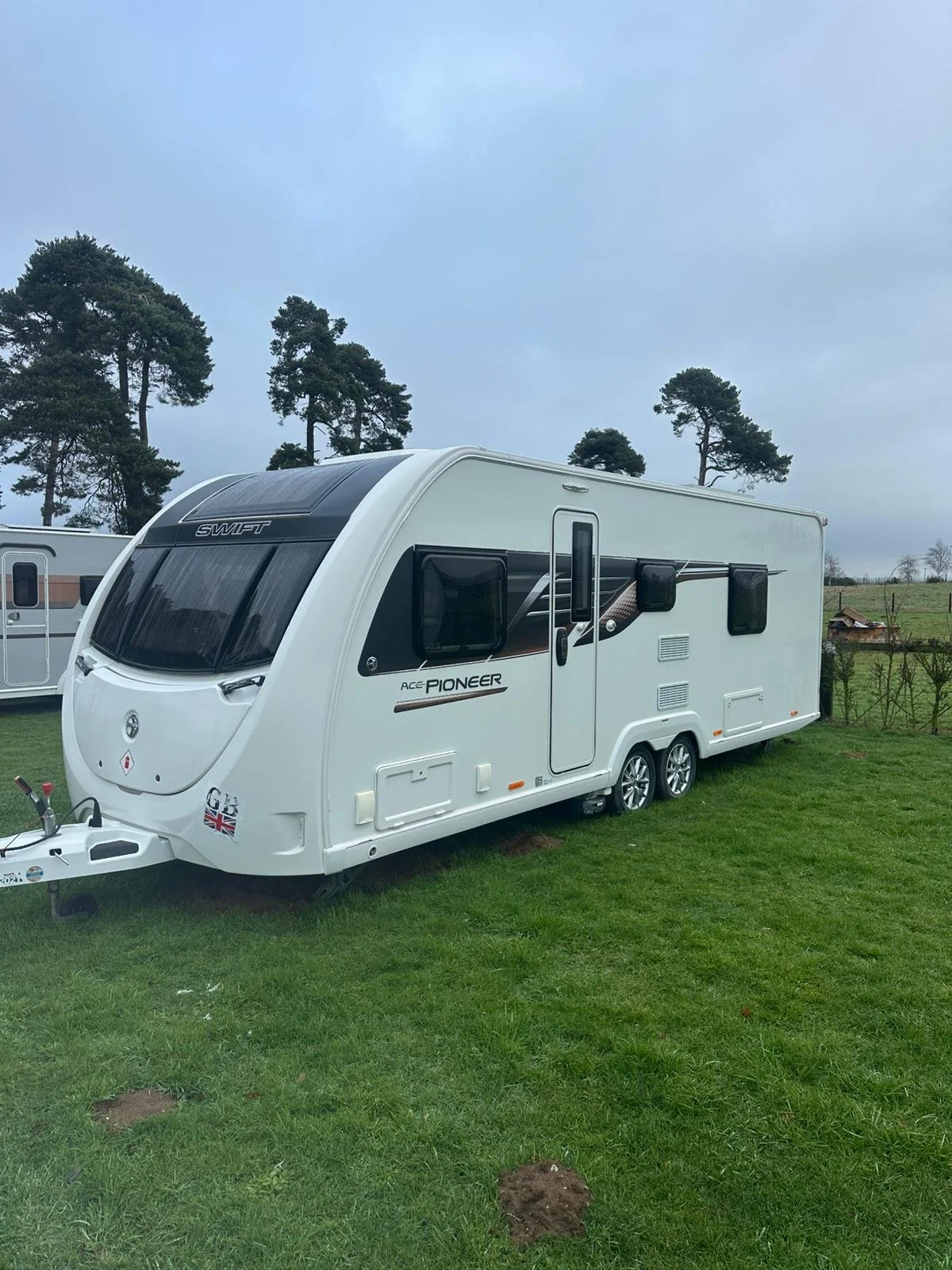 A white travel trailer parked on green grass with trees and cloudy sky in the background.