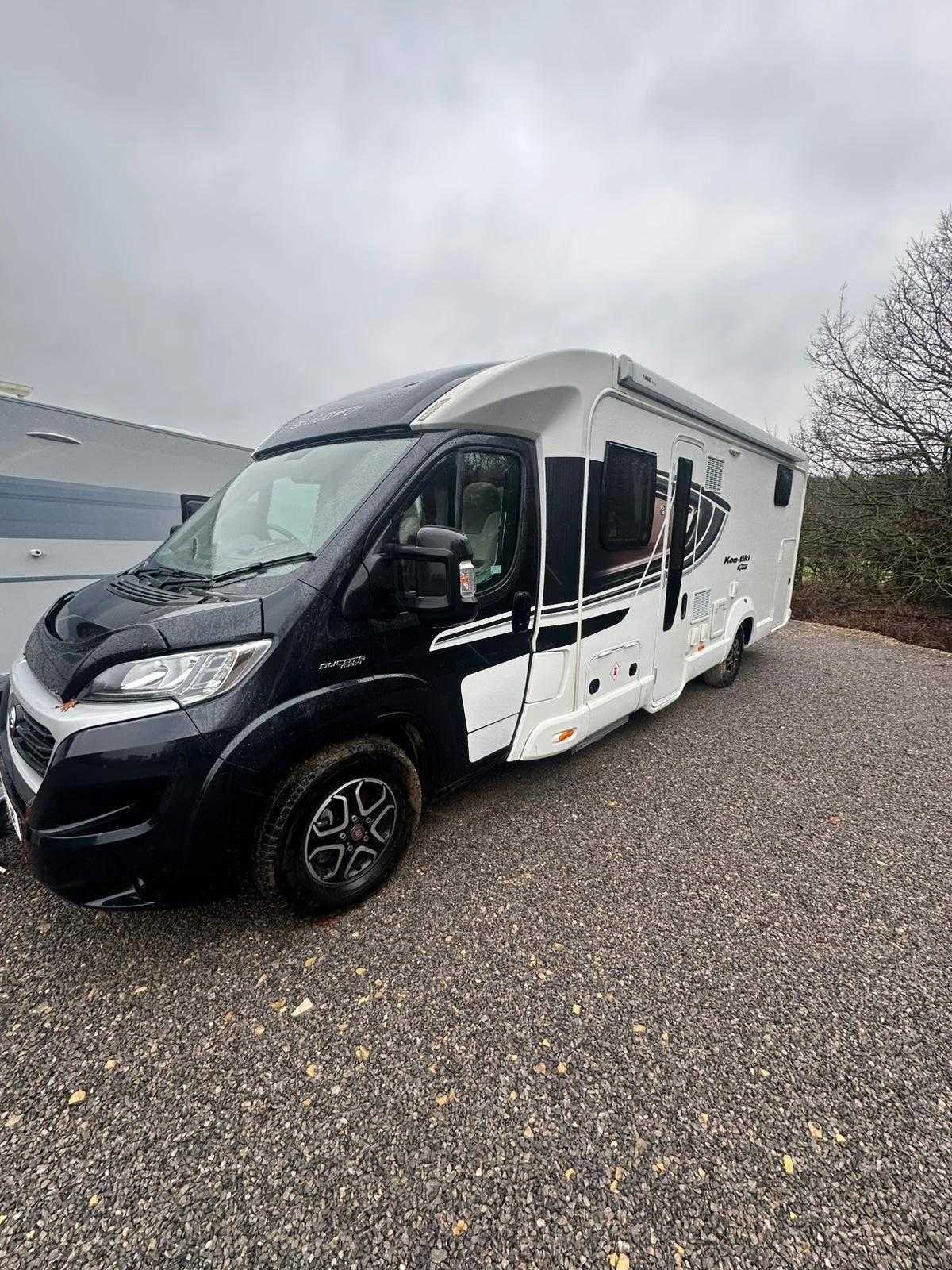 A black and white motorhome parked on a gravel lot under a cloudy sky.