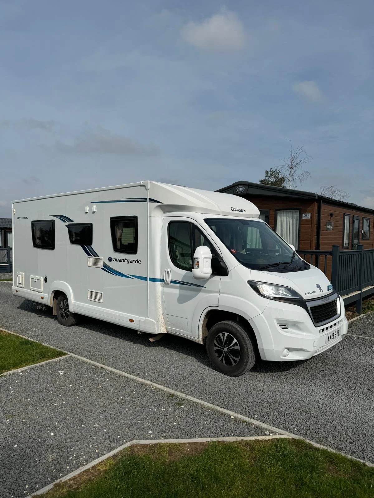 A white motorhome parked on a gravel driveway next to a wooden building.
