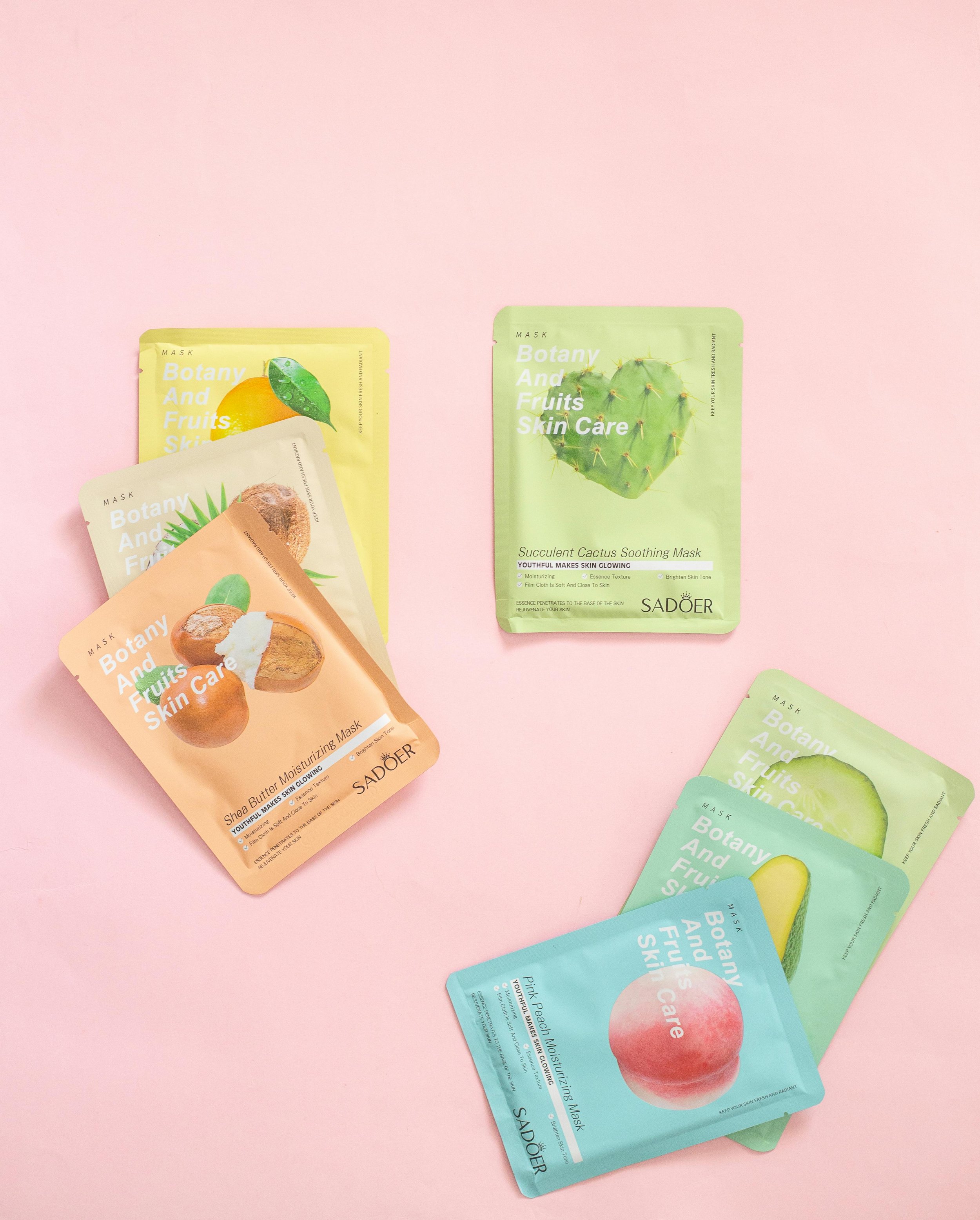 Varias mascarillas faciales de diferentes sabores y ingredientes con colores pastel sobre un fondo rosa.