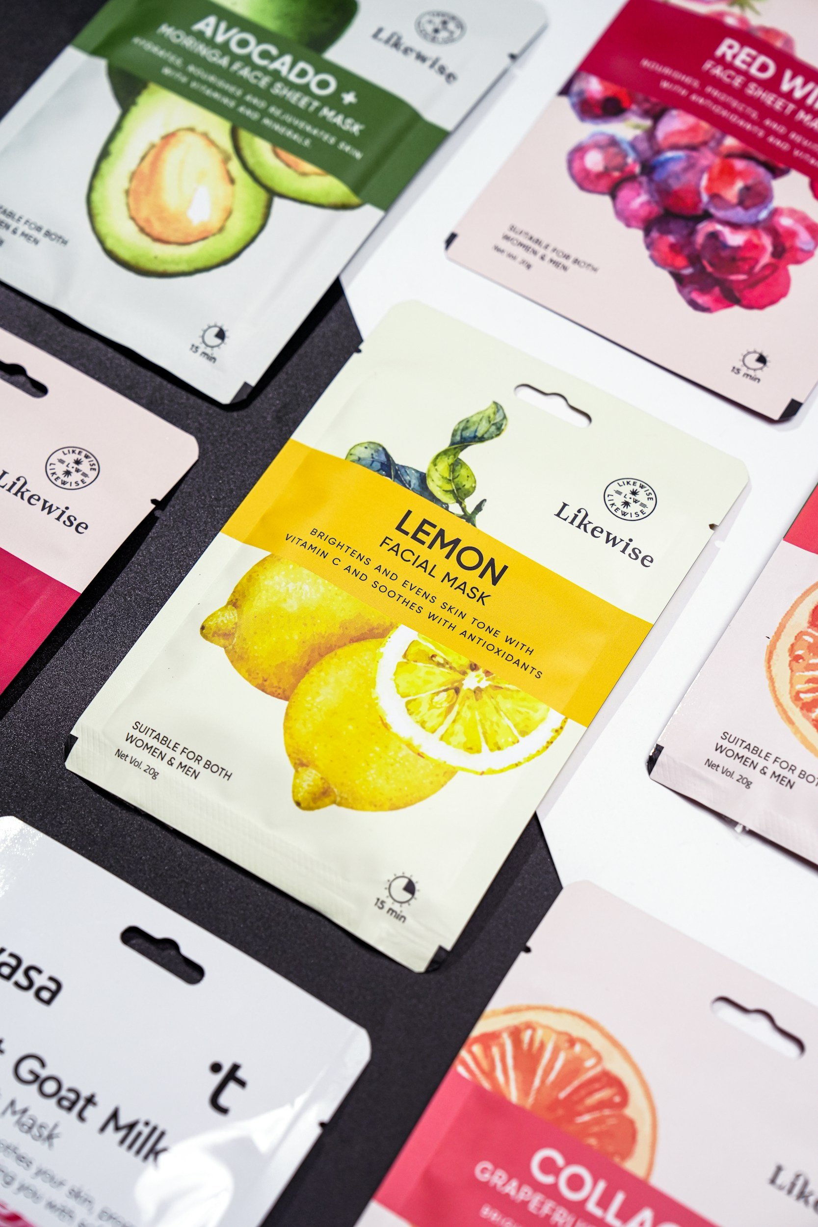Varias mascarillas faciales en paquete, incluyendo una de aguacate, una de limón, una de frutos rojos, y otras de diferentes ingredientes con colores vivos y diseños ilustrativos.