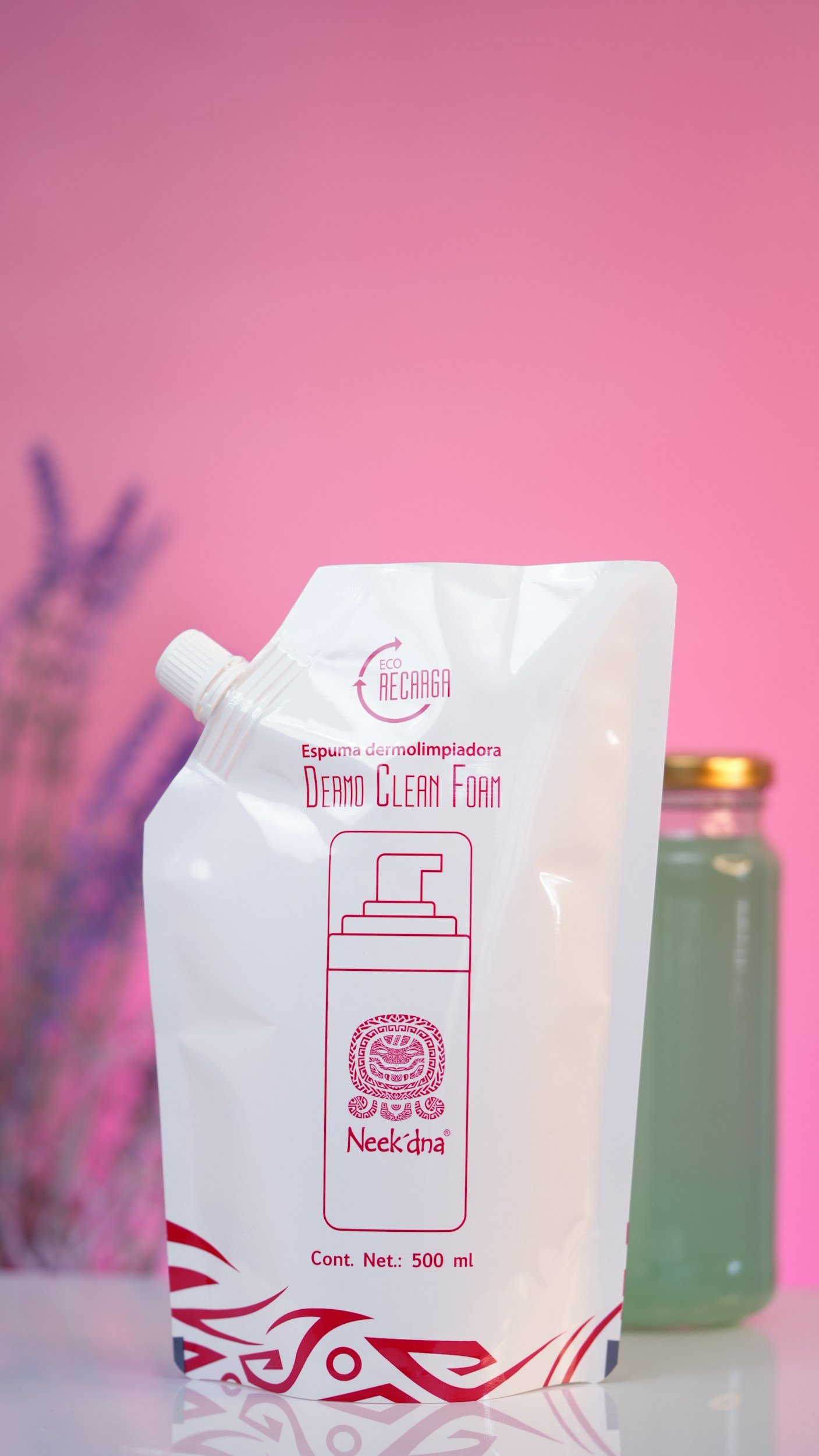 Paquete de espuma dermolimpiadora Neo Clean Foam con diseño en color blanco y detalles en rojo, sobre fondo rosa con jarra de vidrio y plantas en el fondo