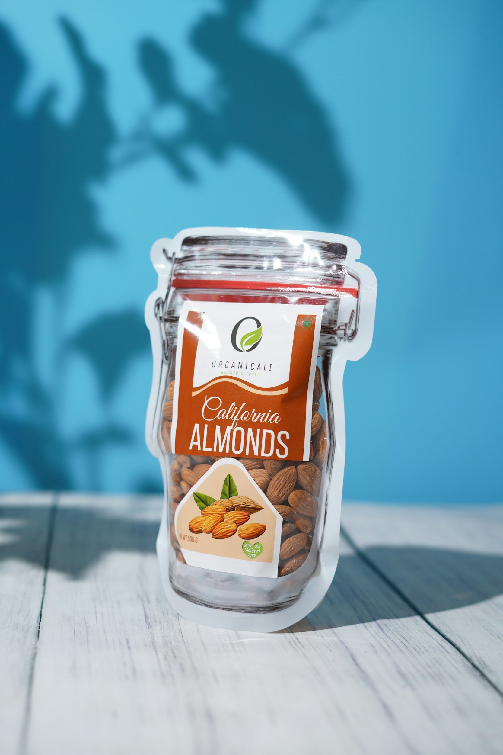 Paquete de almendras orgánicas de California en un fondo azul con sombra de hojas.