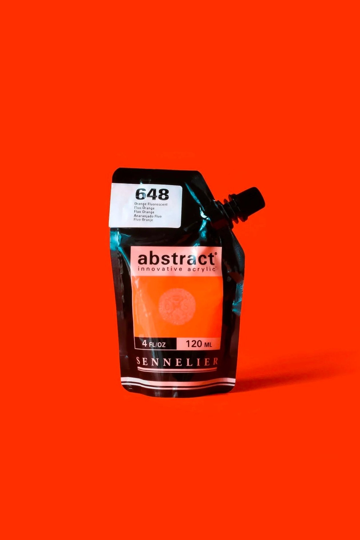 Envase de pintura de color naranja fluorescente en una bolsa con tapa de rosca y etiqueta que dice 'abstract' y 'Sennelier', con fondo naranja.