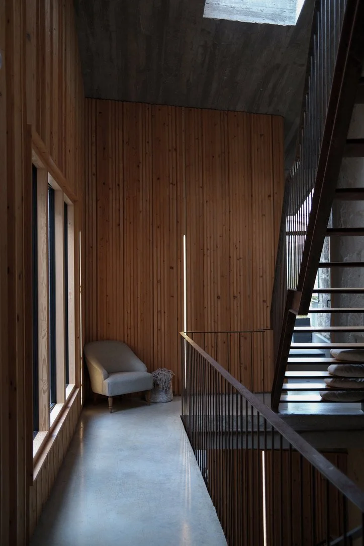 A modern interior space with wooden panel walls, a beige armchair, a small table, and metal staircase railing.