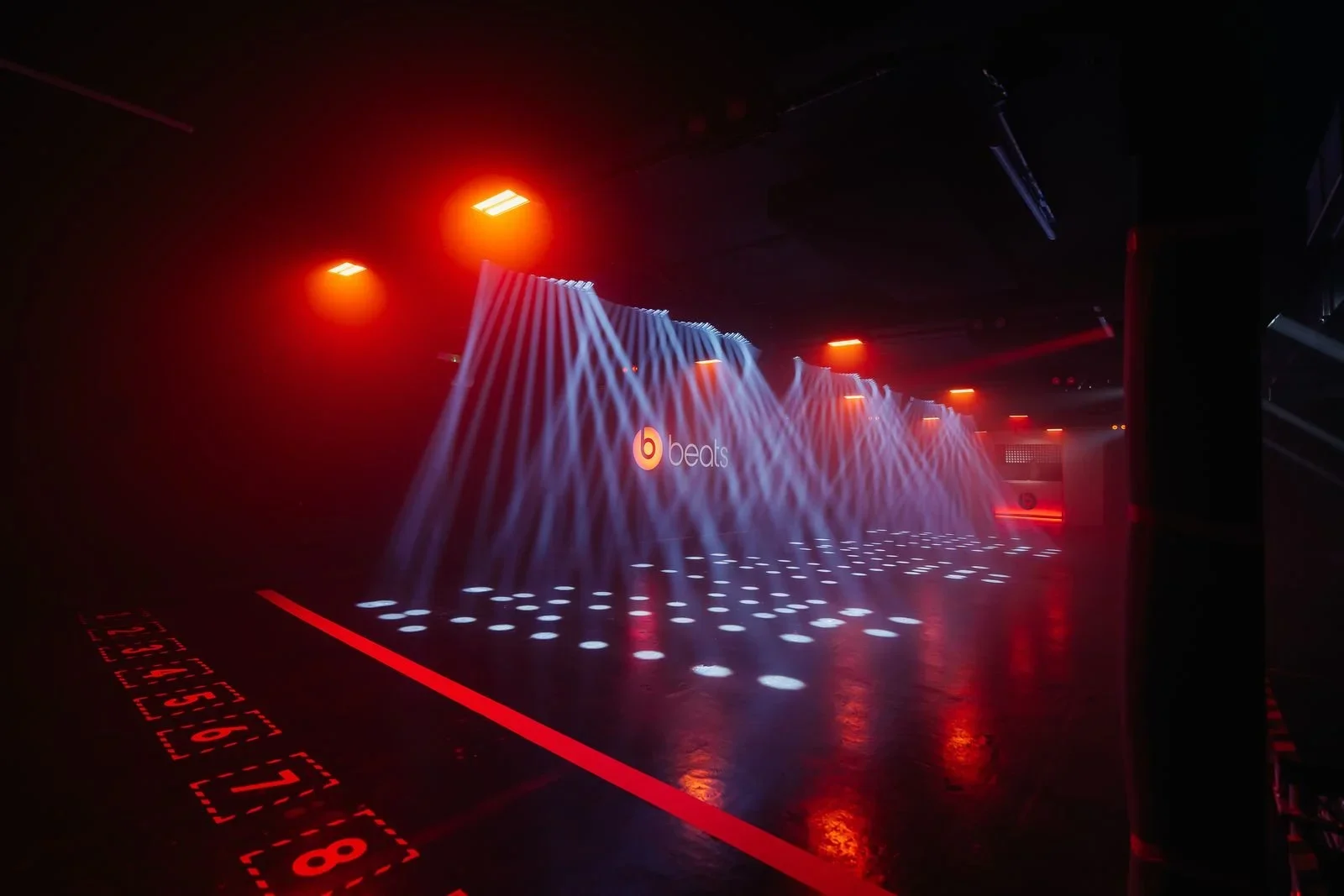 A nightclub dance floor with blue and red lighting, a backdrop displaying the Beat logo, and a grid of white circular lights on the floor.