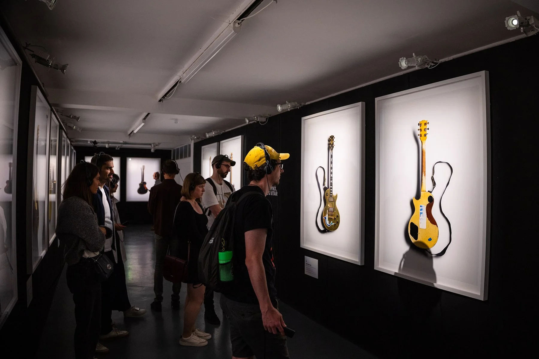 People viewing framed artwork of musical guitars in an art gallery.