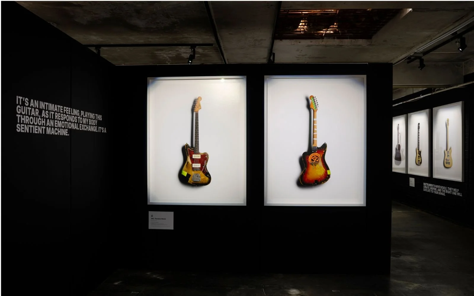 Exhibition of vintage electric guitars displayed on white backgrounds in a dark gallery.