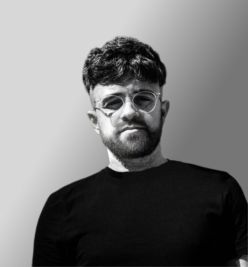 Black and white photo of a man with glasses, a beard, and short hair, wearing a plain dark t-shirt.