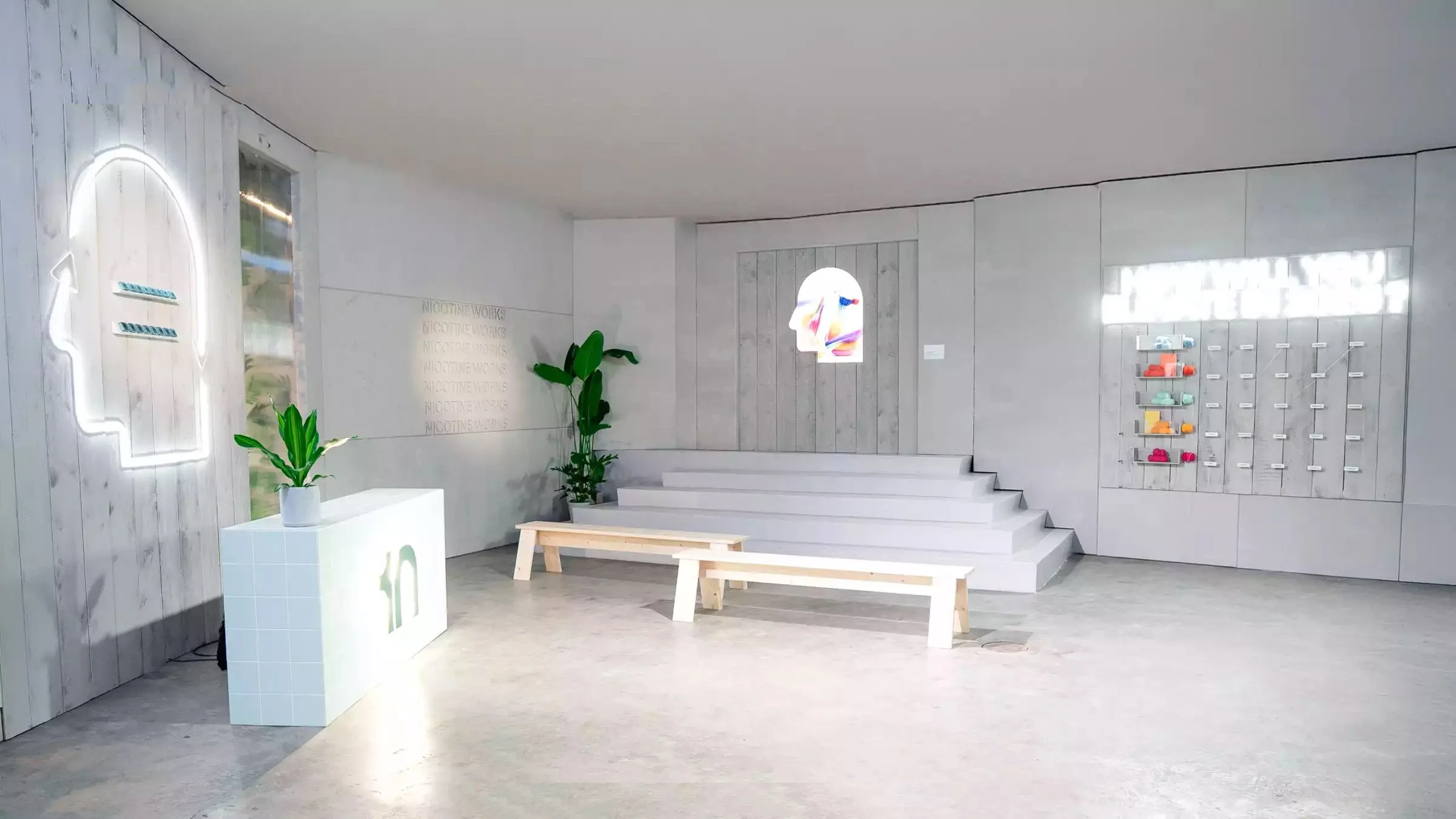 Modern minimalist lobby with white stairs, wooden benches, potted plants, and wall decor in pastel colors.