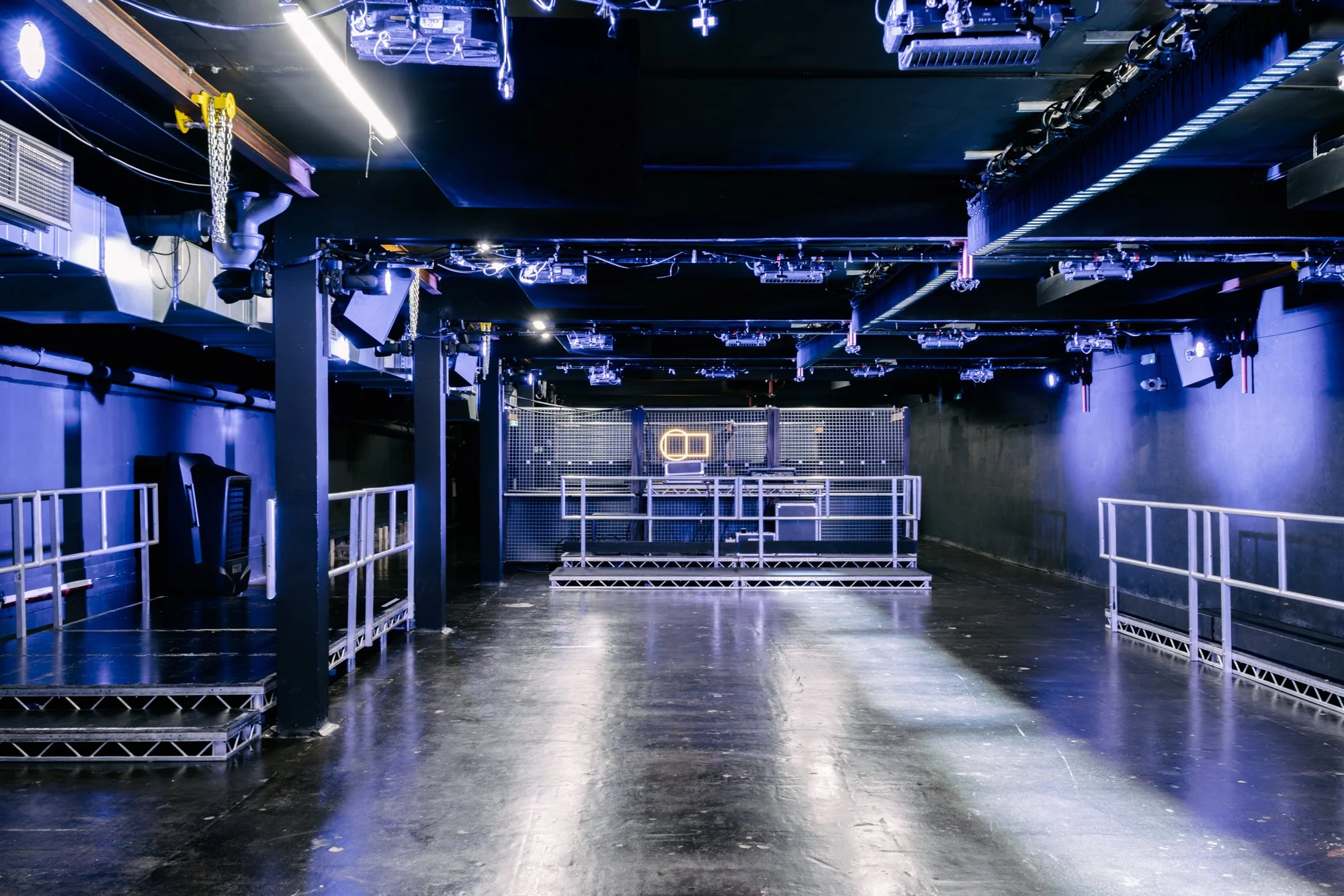 Empty nightclub or concert venue with stage, scaffolding, and lighting equipment overhead.