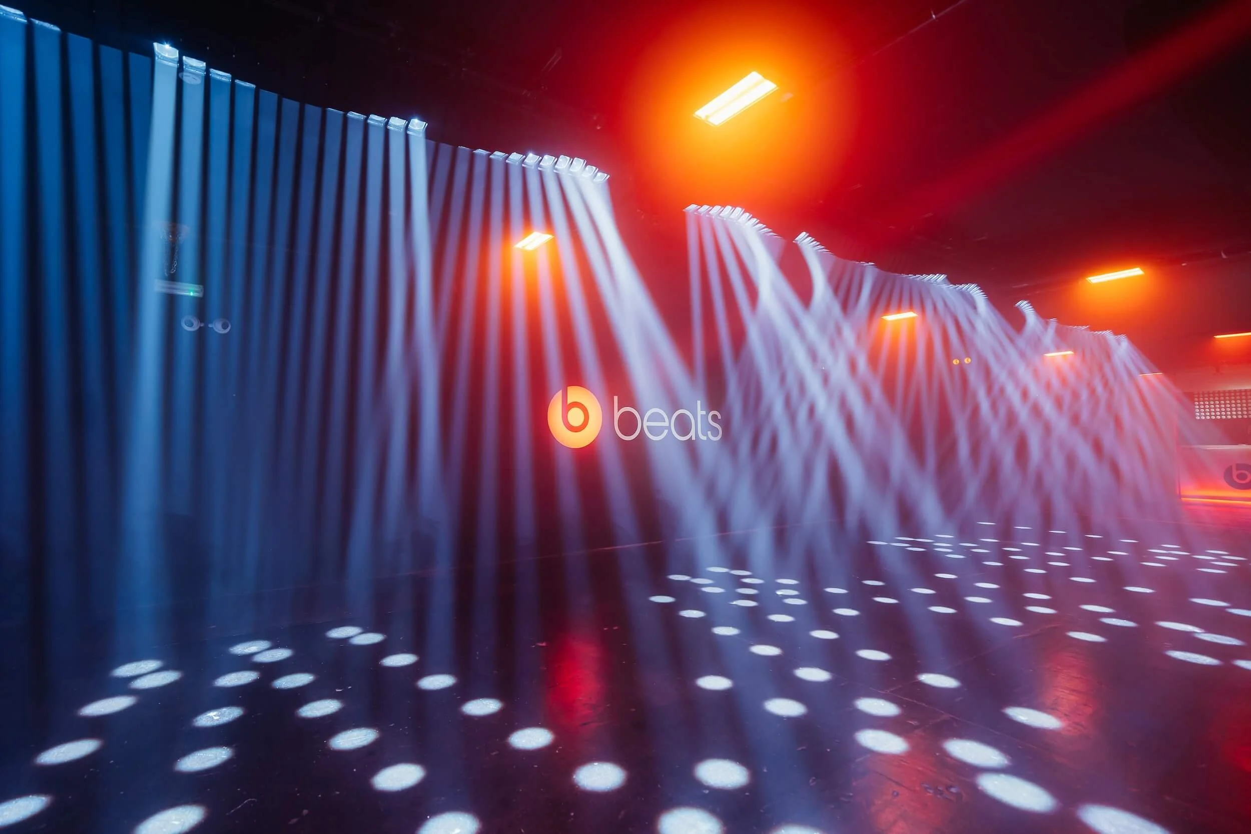 An empty nightclub dance floor with blue and red lighting, white spotlights on the floor, and the 'beats' logo on the wall.
