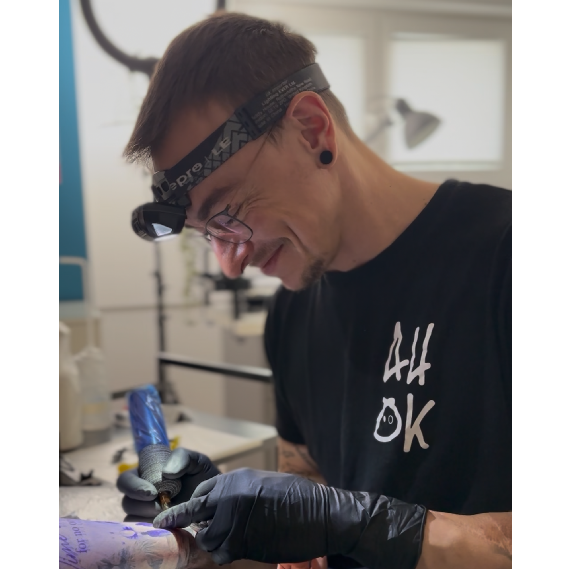 Mann mit Brille, Headlamp und schwarzen T-Shirt beim Tätowieren.