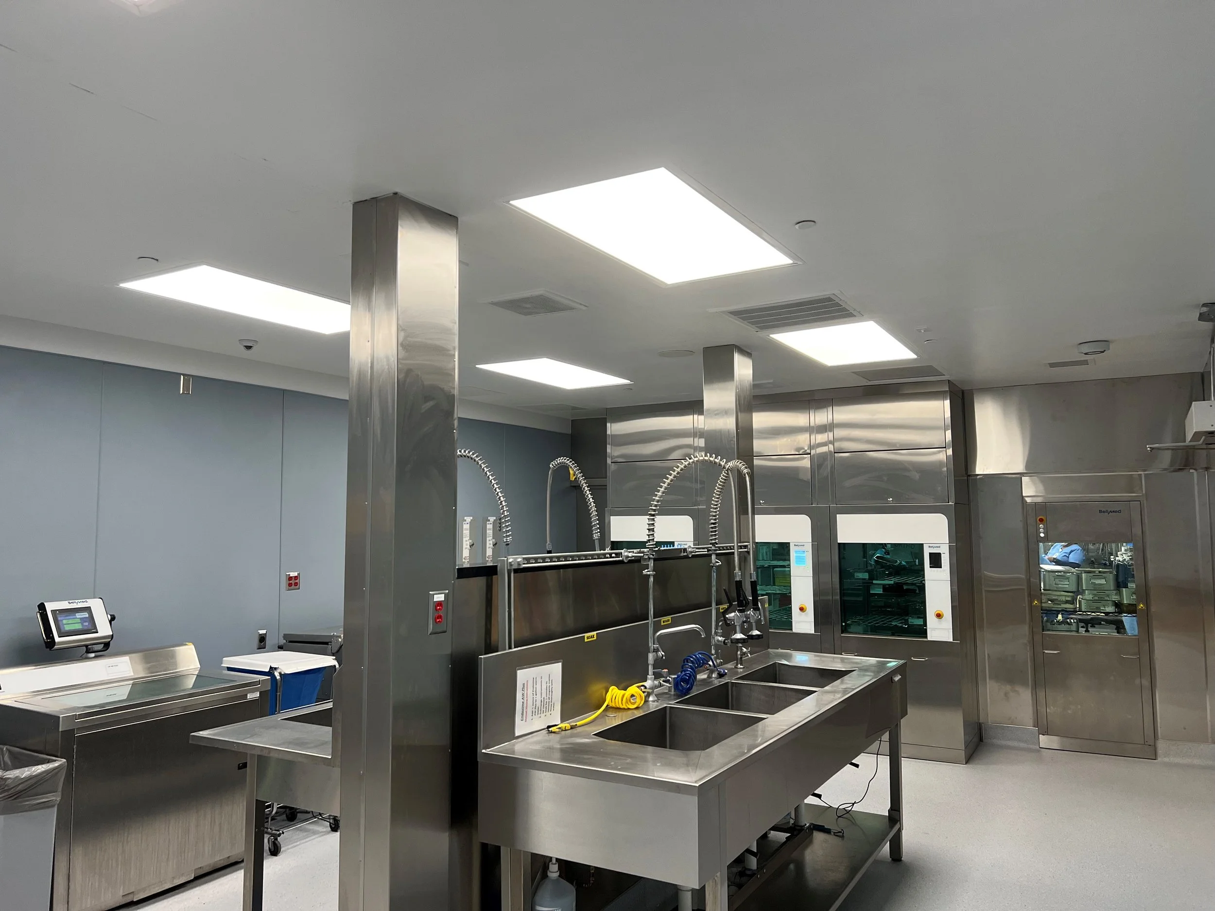 Sterile Processing Unit (SPD) with stainless steel sinks, medical equipment, and blue-gray wall panels.