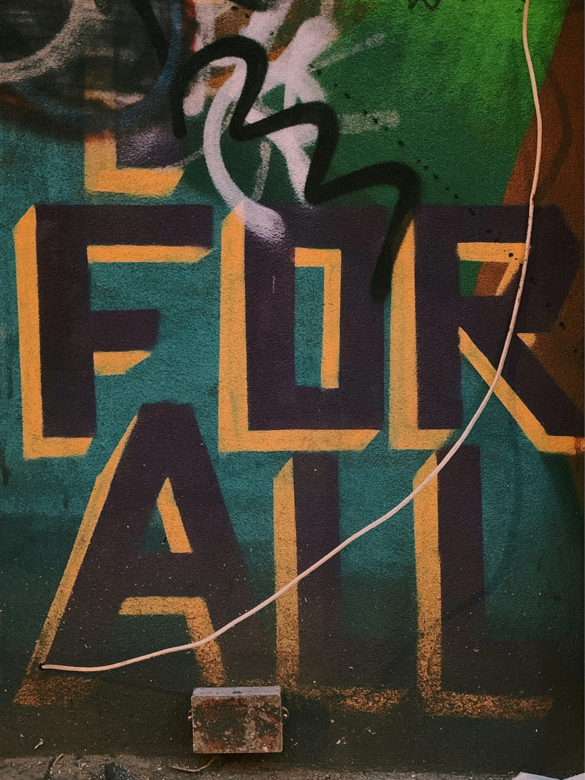 Colorful graffiti wall with the words "FLOW ART" in large block letters, with black and orange outlines, on a green and multicolored background.