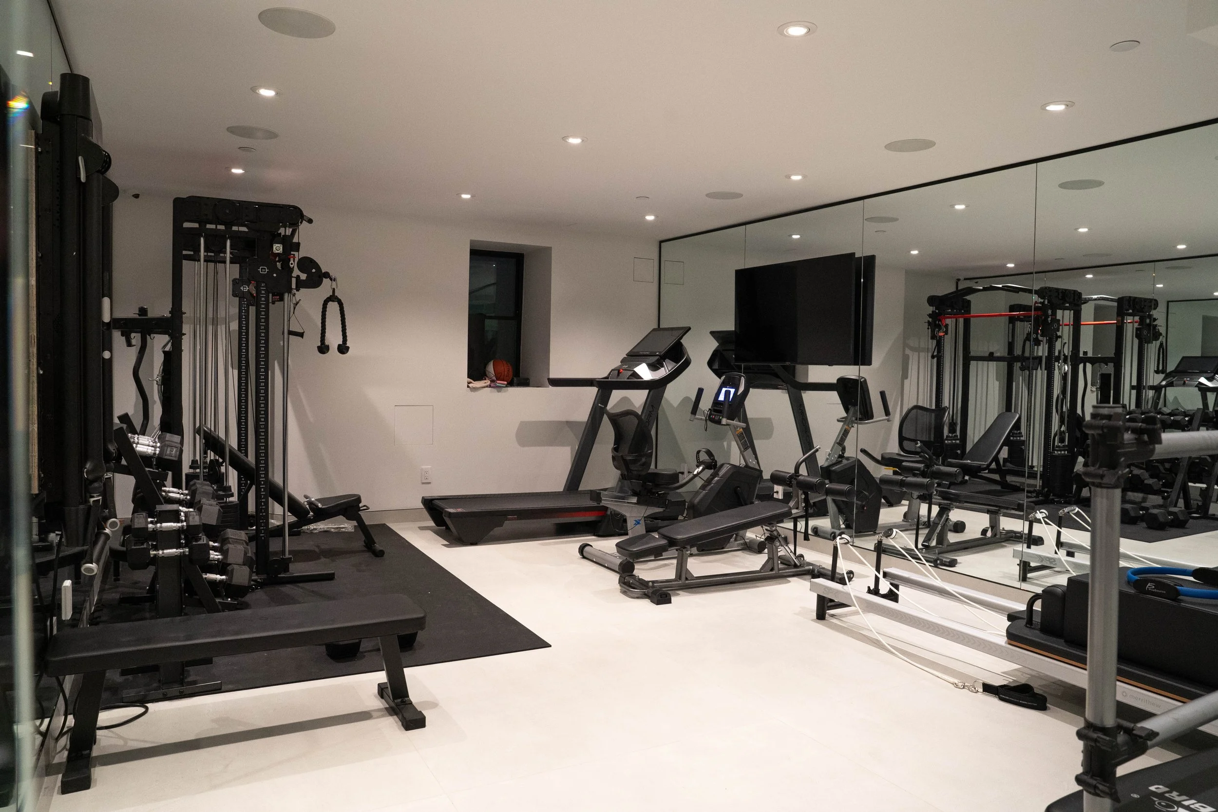 Modern home gym with various exercise equipment including treadmills, elliptical machines, weight machines, dumbbells, and a mirror wall.