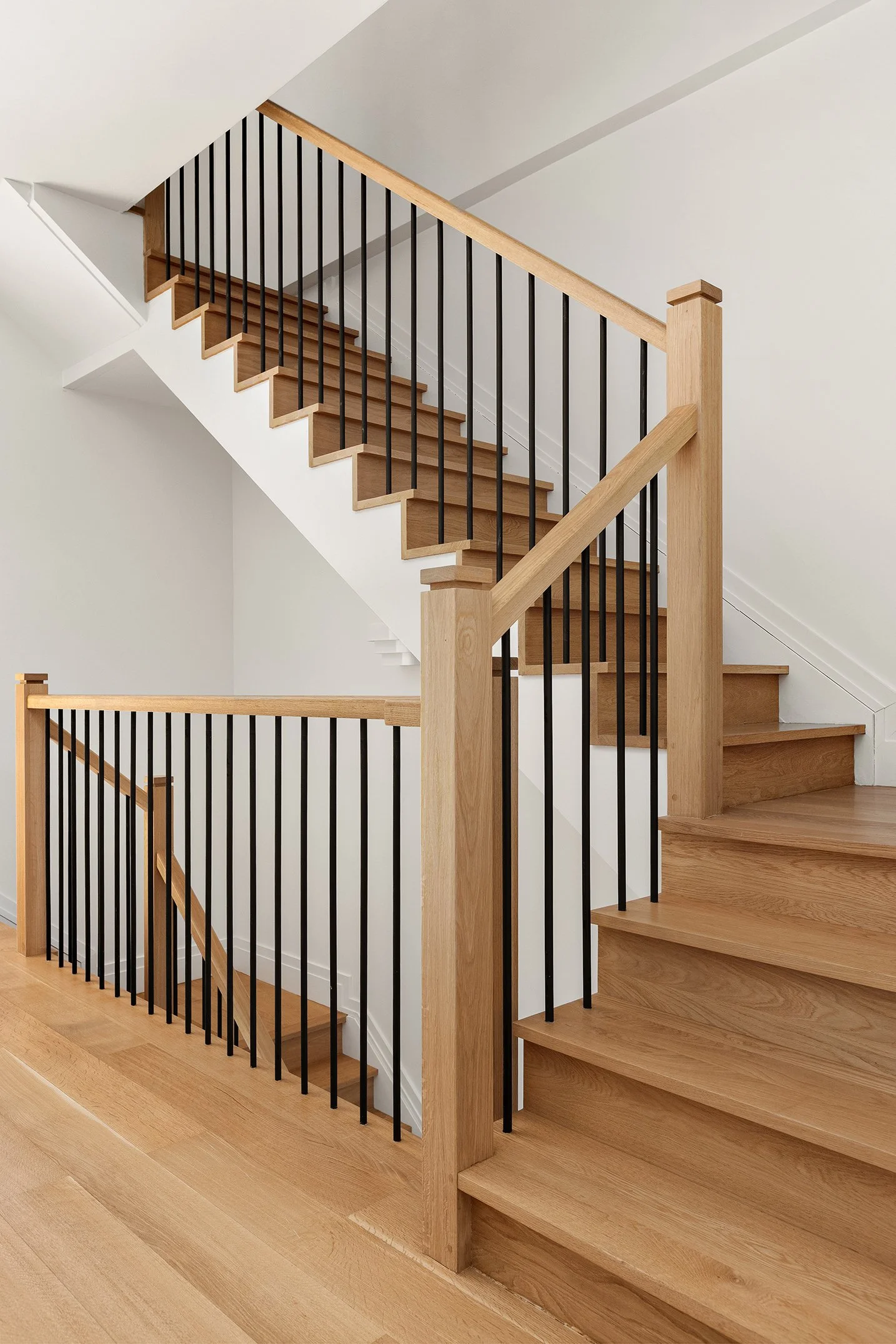 A modern staircase with wooden steps, black metal railings, and a wooden handrail inside a house.