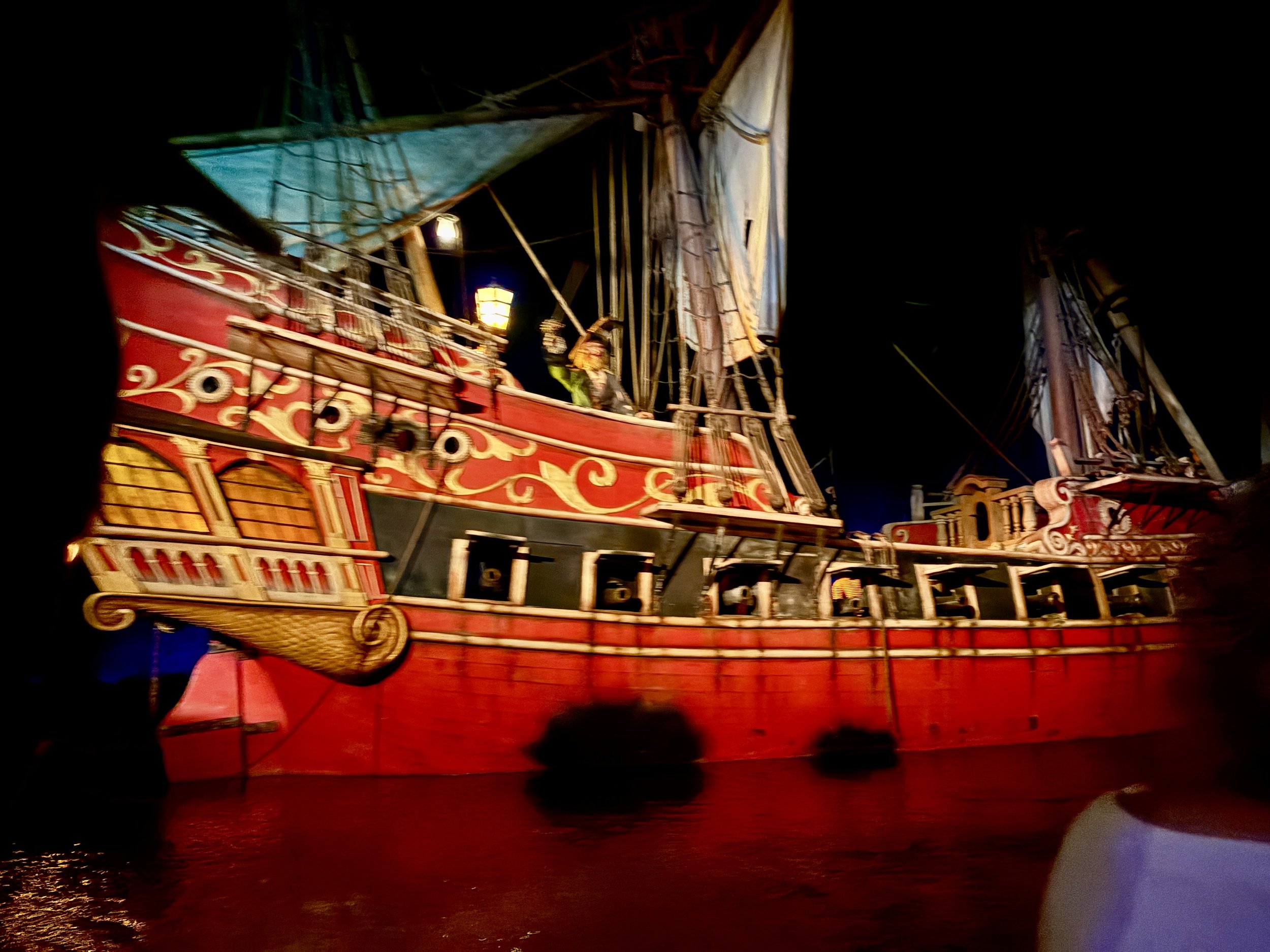A large, elaborately decorated pirate ship prop with red, gold, and black accents, sails at night with lights and a dark sky in the background.