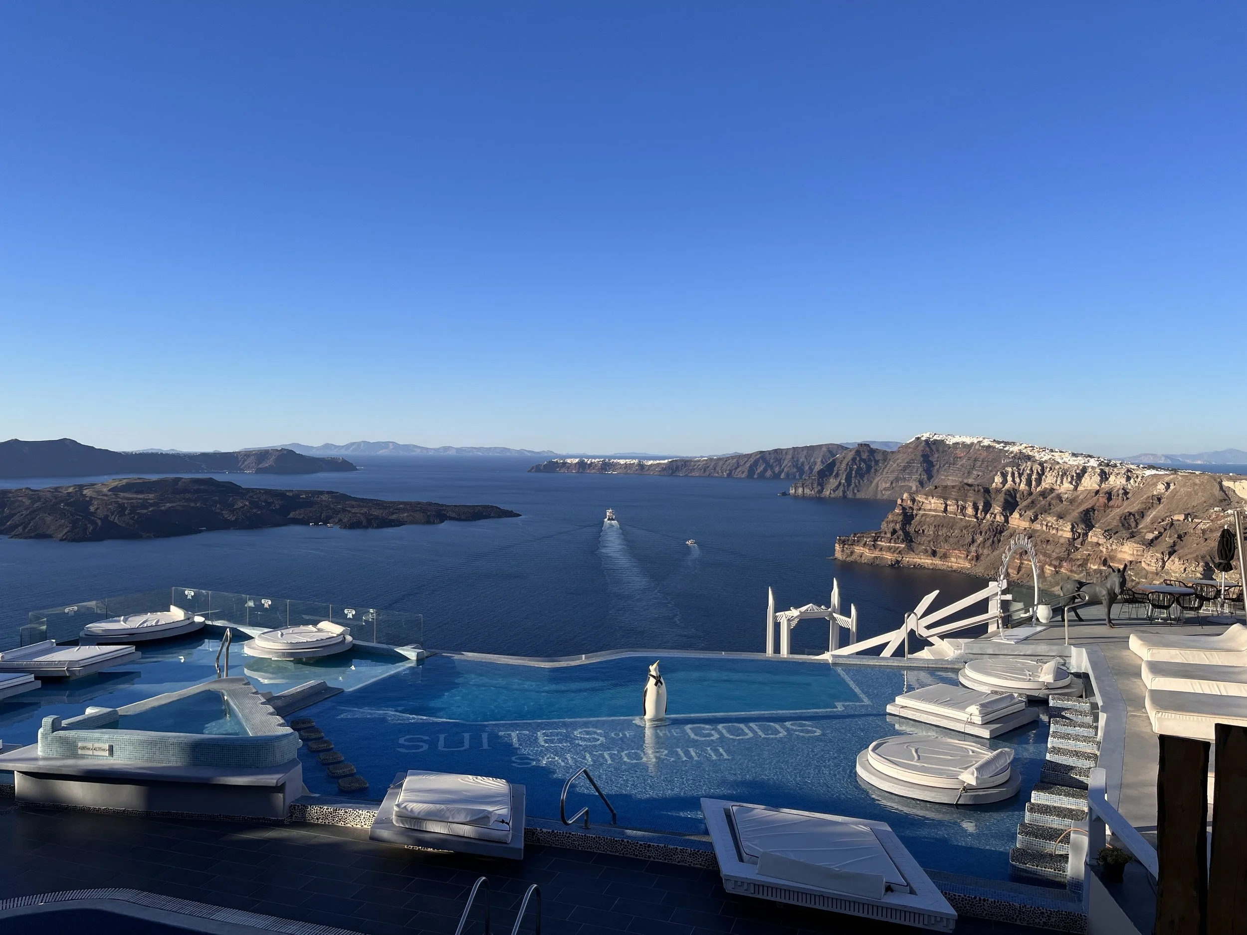 Infinity pool overlooking the caldera in Santorini, Greece, with views of the Aegean Sea and volcanic cliffs on a clear day.