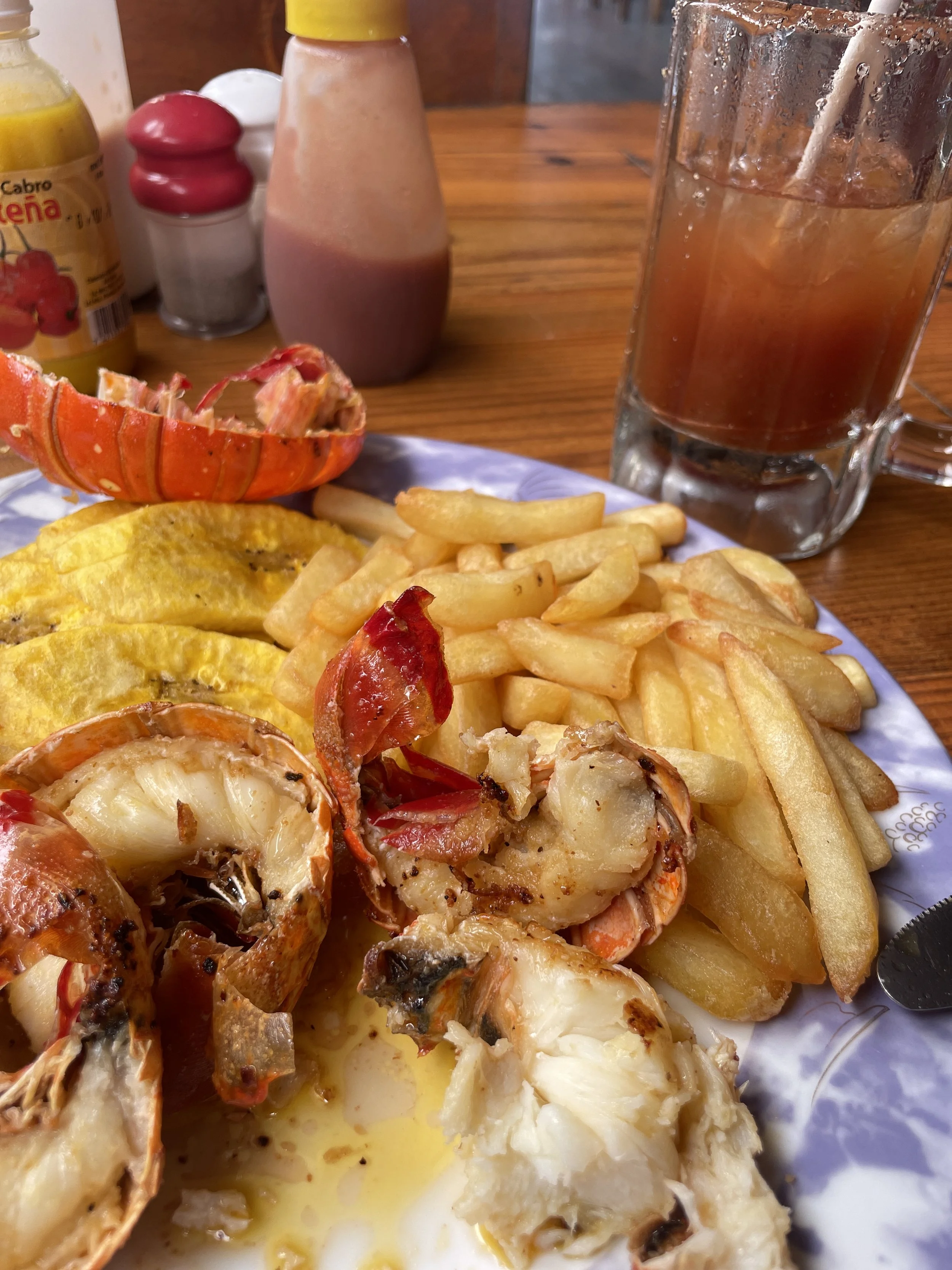 Seafood dish with lobster and eggs, served with French fries and a lobster tail, accompanied by a glass of iced tea on a wooden table.