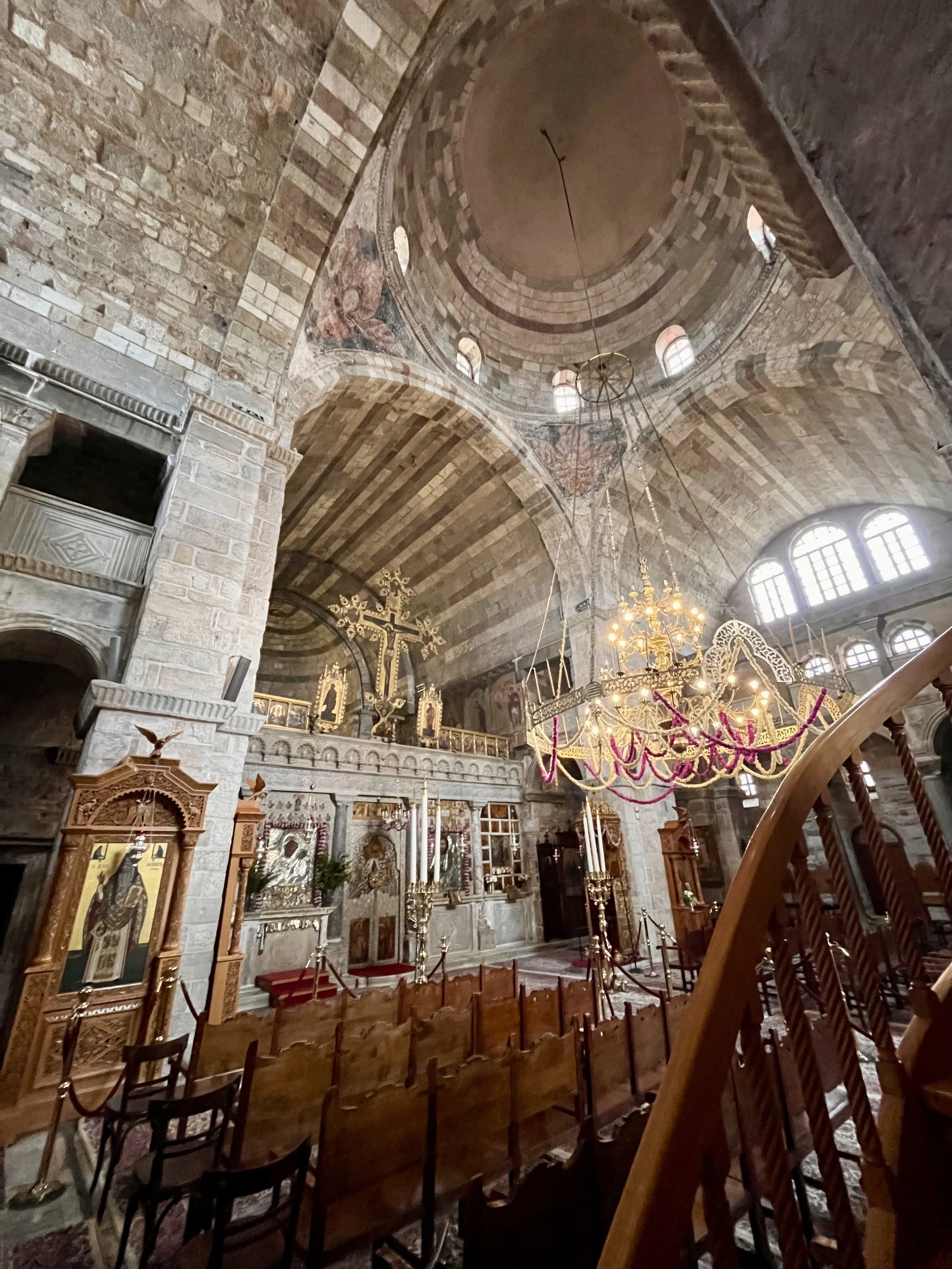 Interior of a historic church with stone walls, a vaulted ceiling, an ornate chandelier, and religious icons and symbols on the altar.