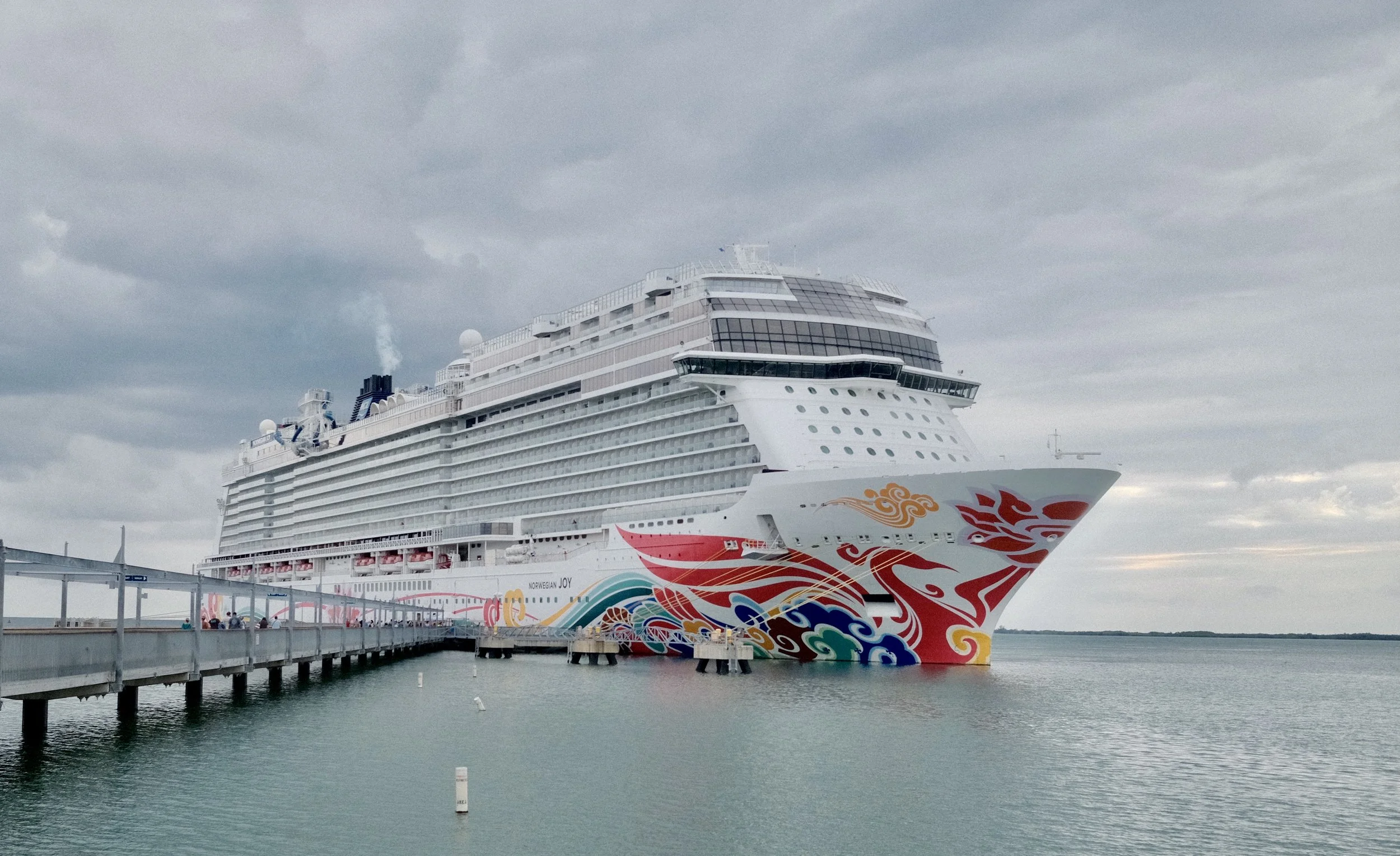 Large cruise ship docked at a pier in cloudy weather with colorful wave and dragon designs on its hull.
