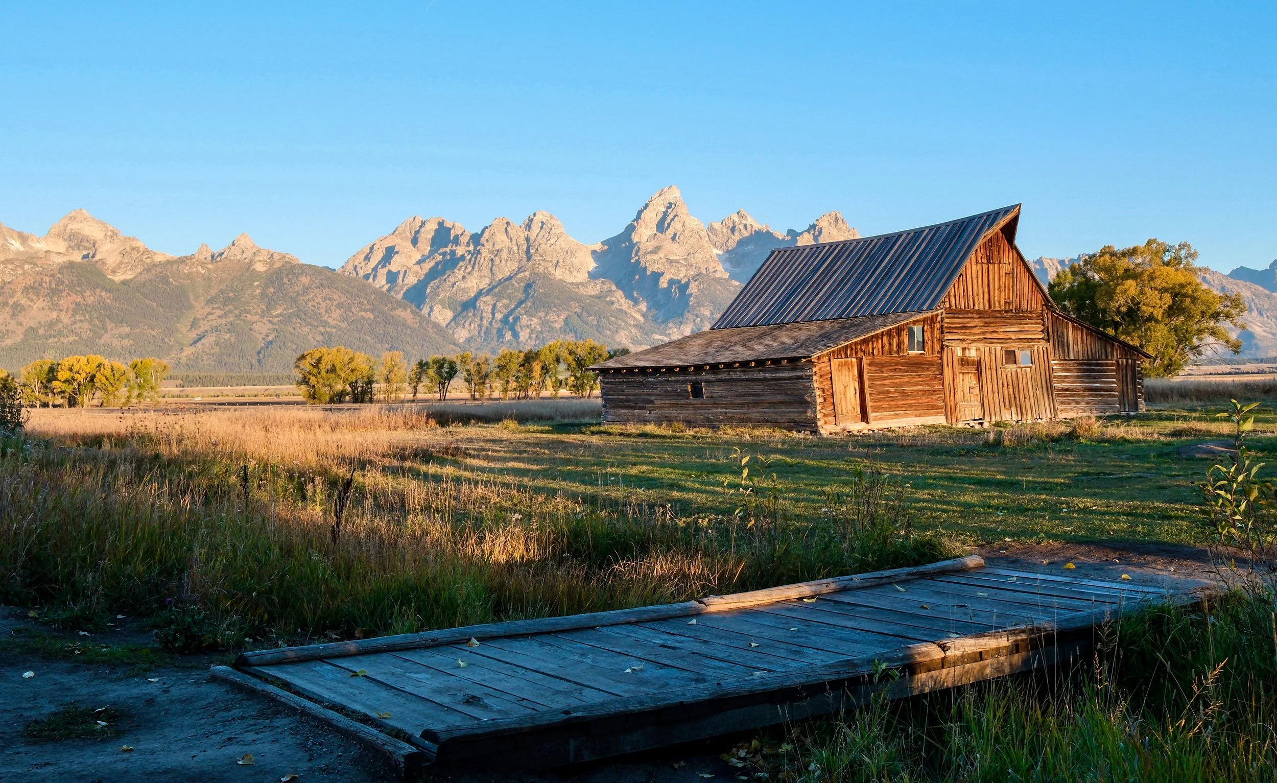 An old wooden barn in a field with mountains in the background at sunset.