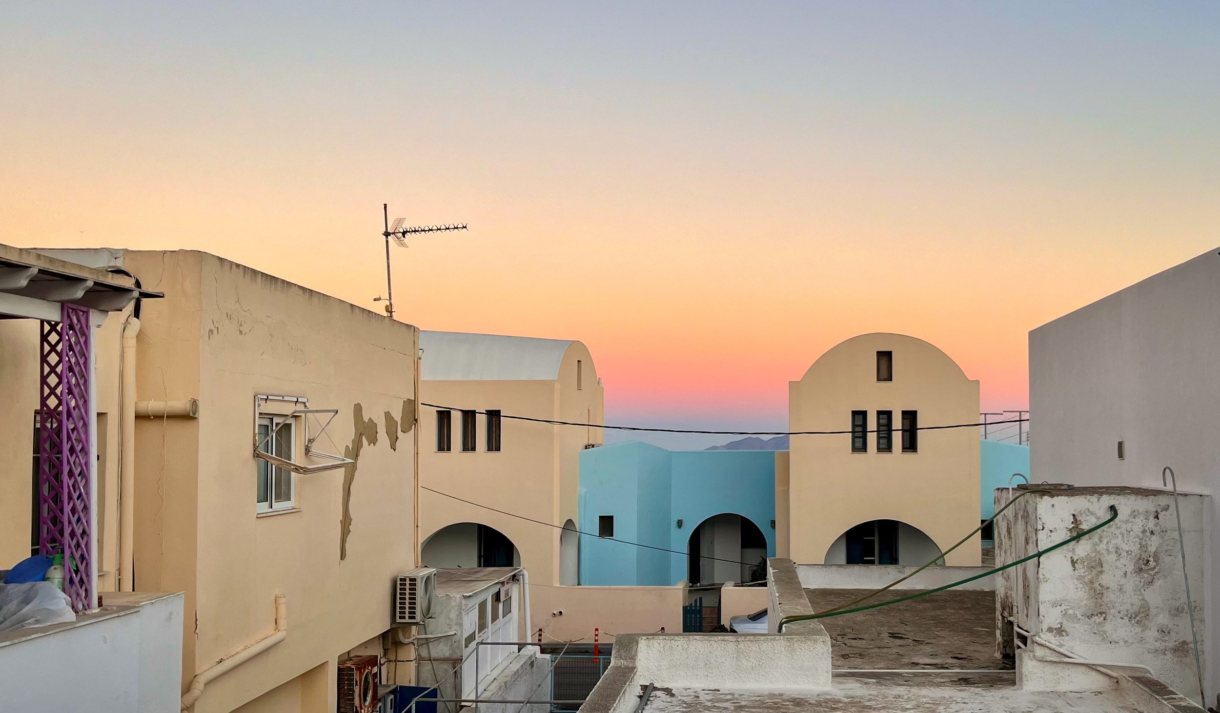 Sunset over Mediterranean-style buildings with pastel colors, arched windows, and flat rooftops.