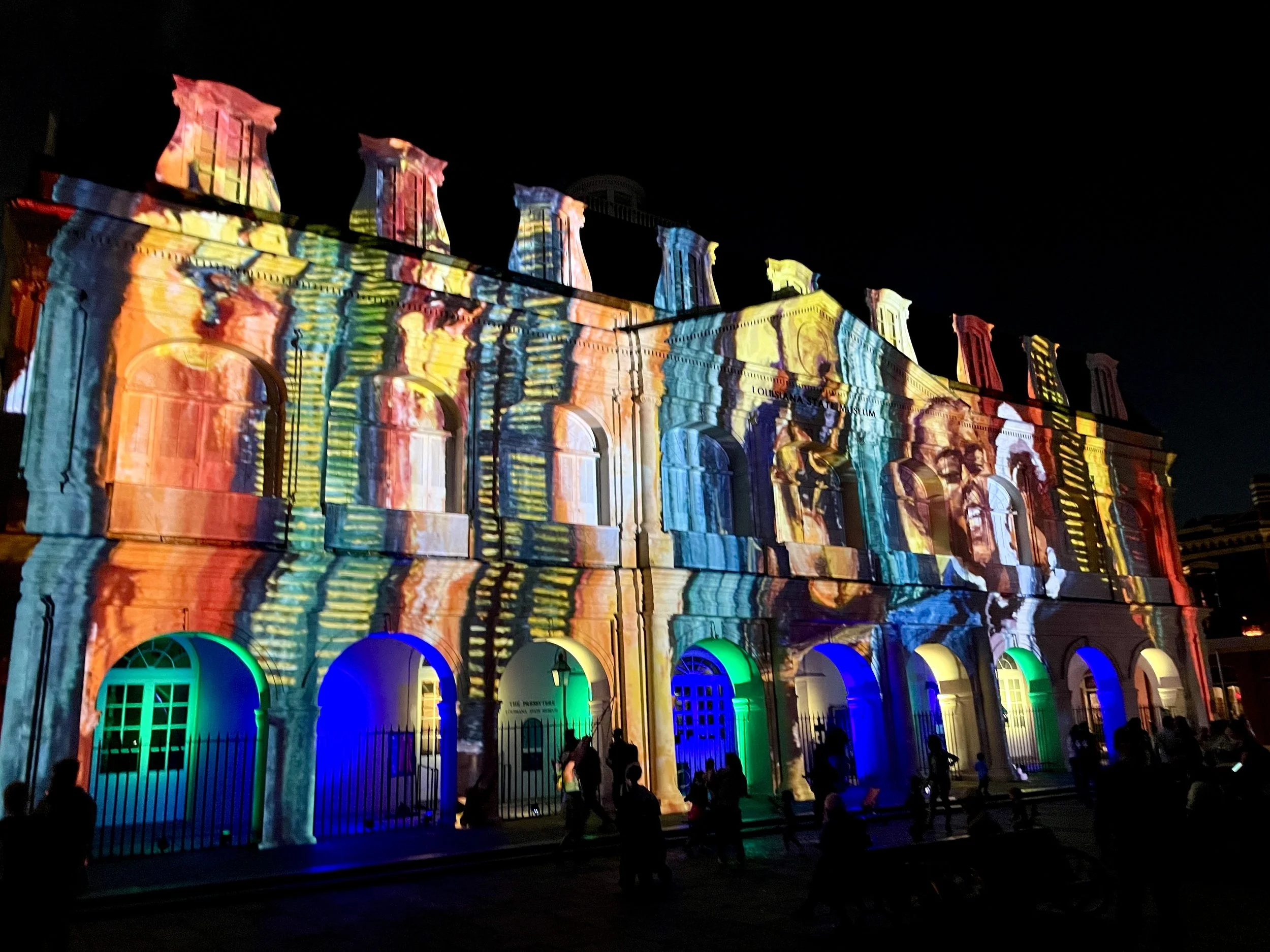 Building illuminated with a colorful light projection at night, featuring arches and architectural details.